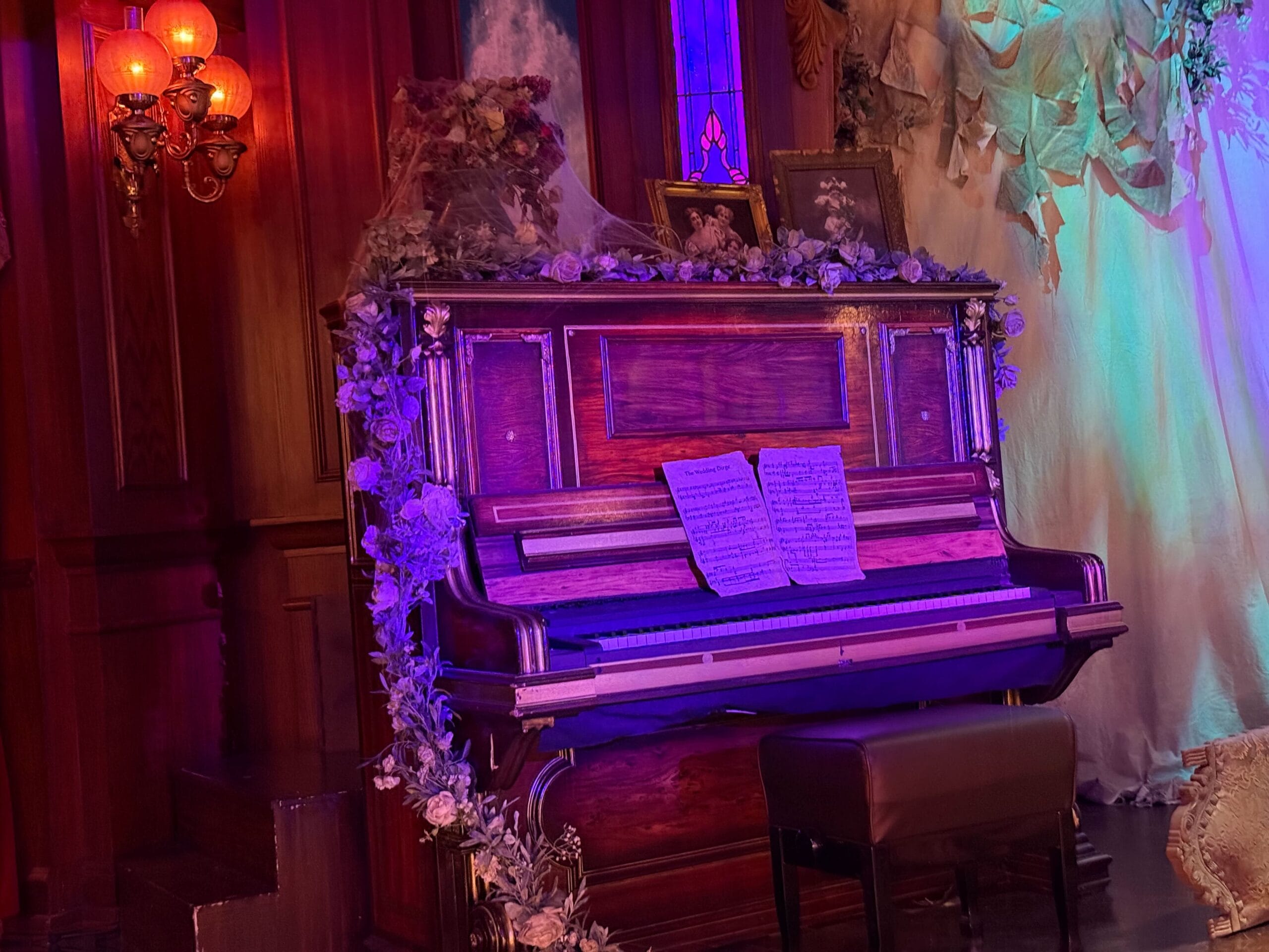 An old upright piano at Phantom Manor, adorned with flowers and sheet music, glows in purple and orange vintage light.