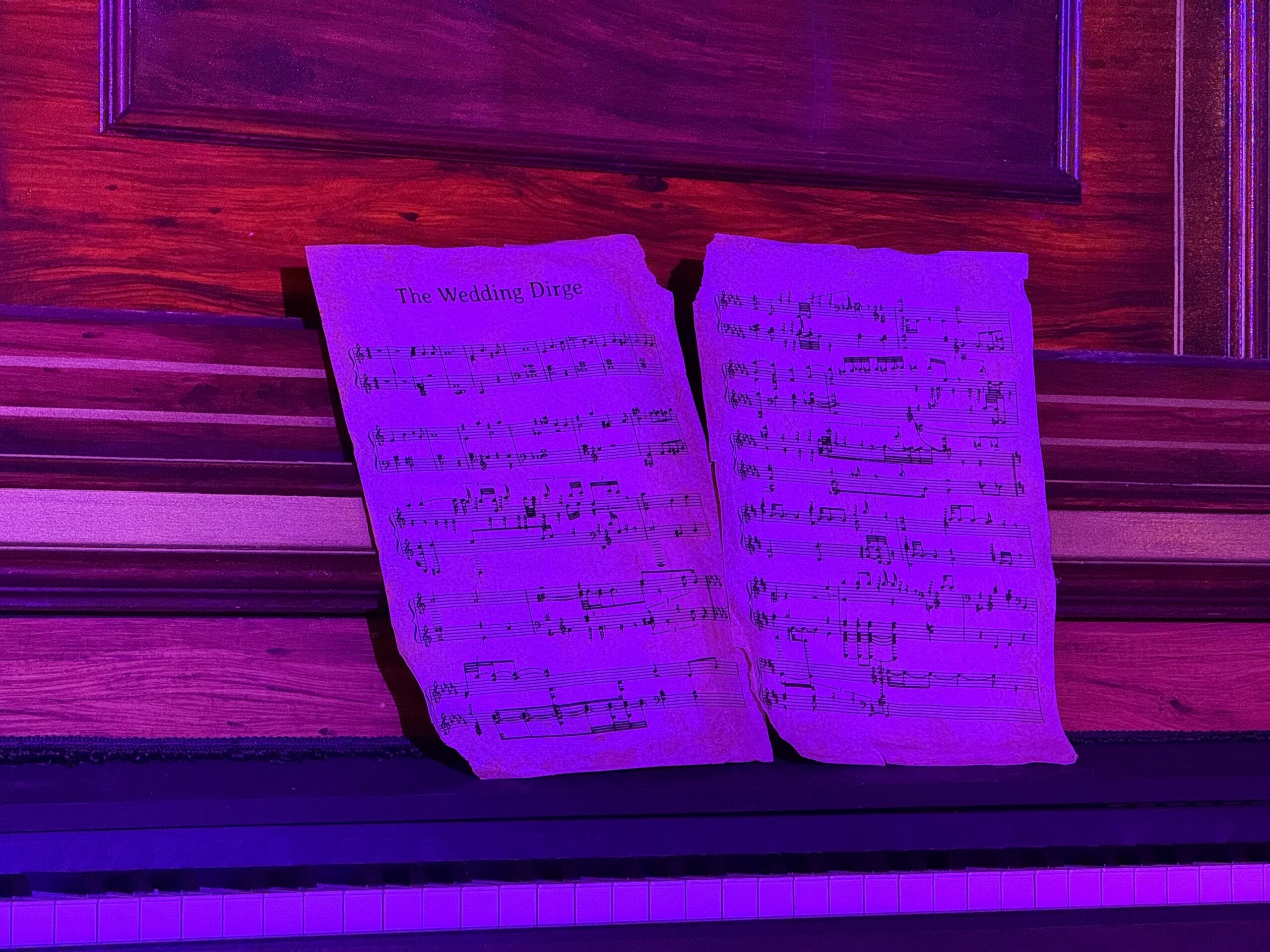 Sheet music titled "The Wedding Dirge" on piano at Unlucky Nugget Saloon, bathed in purple light.