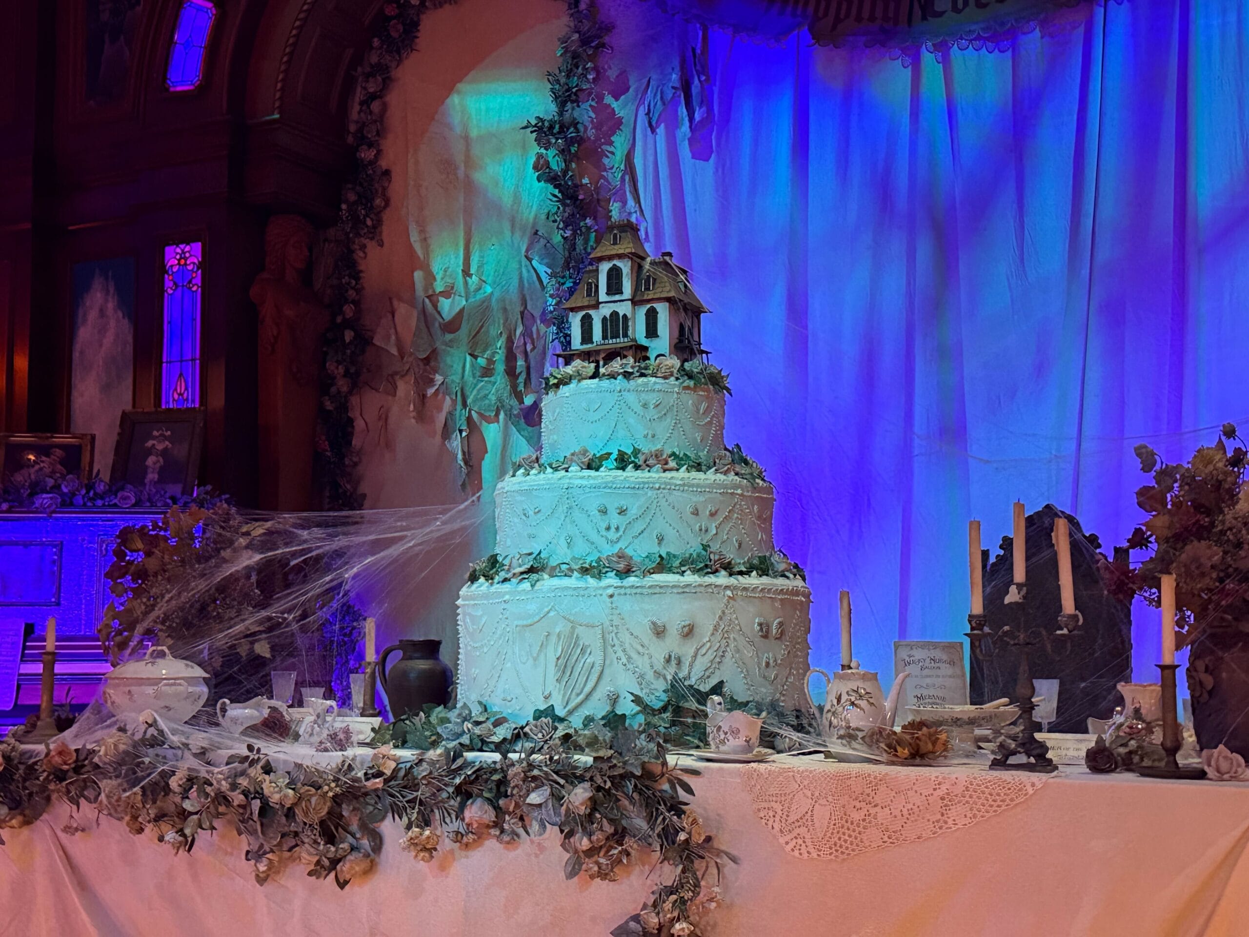 Three-tiered cake with a Phantom Manor haunted house topper, cobwebs, candles, and gothic décor inspired by Disneyland Paris.