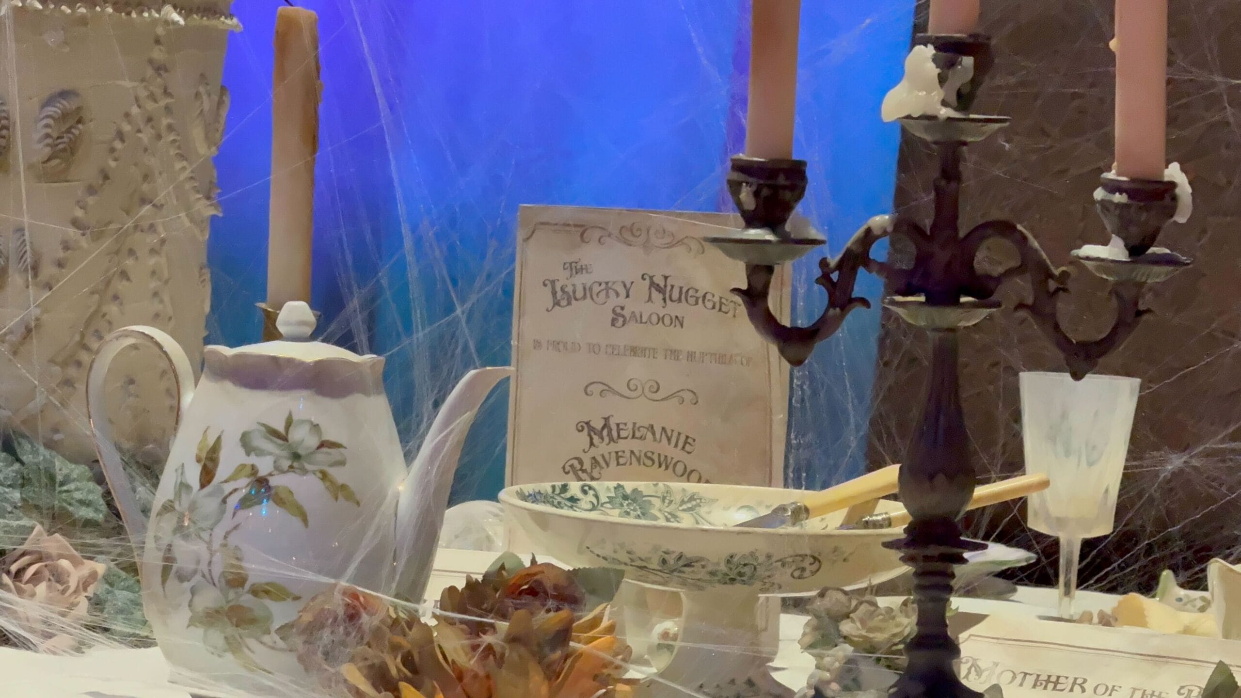 A vintage teapot, candleholder, and menu from Phantom Manor sit on a cobwebbed table at Disneyland Paris.