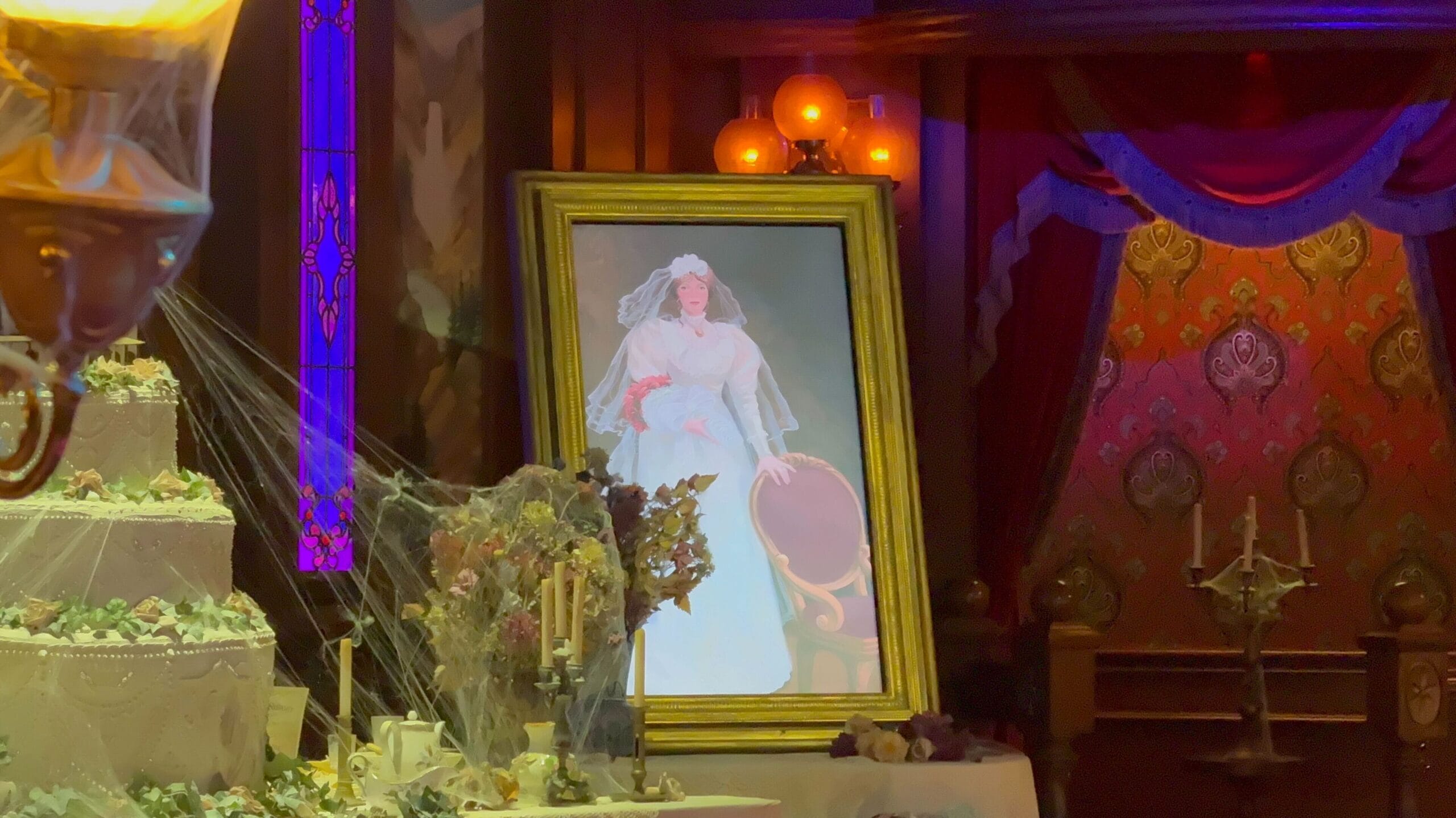 A framed bride’s portrait by a cobwebbed cake in Phantom Manor's eerie, red-draped room at Disneyland Paris.