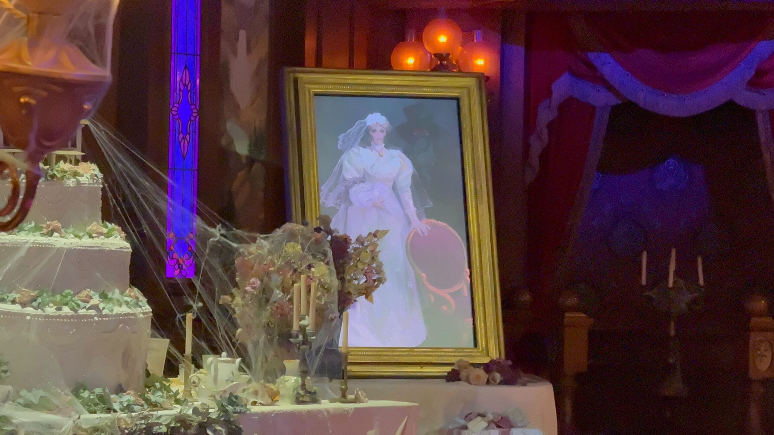 A bride in white stands behind a cobwebbed cake in a dim, eerie room at Phantom Manor, Disneyland Paris.