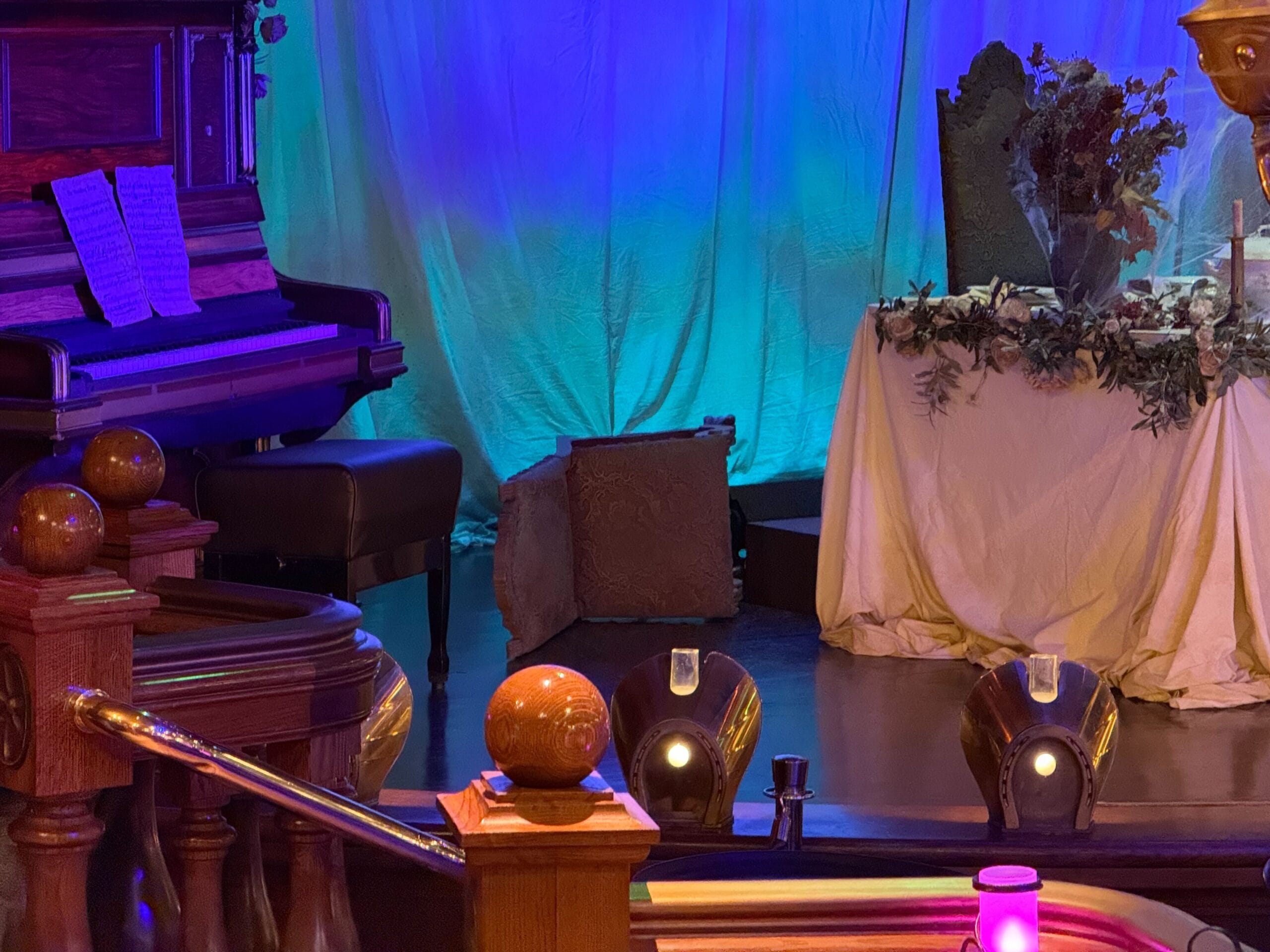 A piano with sheet music sits on a stage at the Unlucky Nugget Saloon, lit by purple and blue lighting.