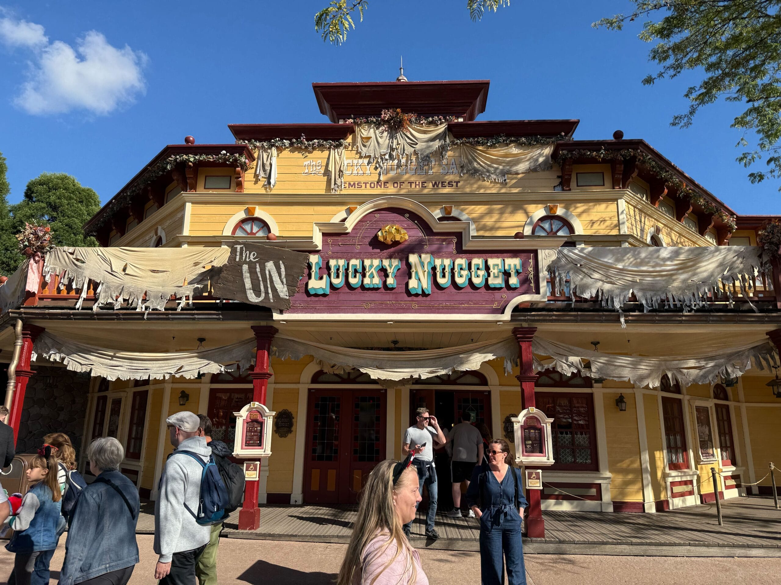 People stroll past The Lucky Nugget Saloon at Disneyland Paris, decked in Halloween decor, near Phantom Manor.