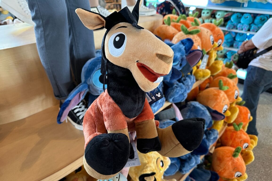 A plush toy horse with a happy expression displayed in a store among other colorful stuffed animals.