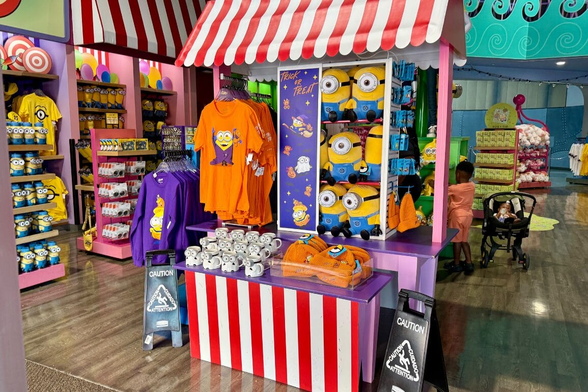Colorful gift shop at Universal Studios Florida with Minions Halloween Collection, shirts, plush toys, and a parent with stroller.