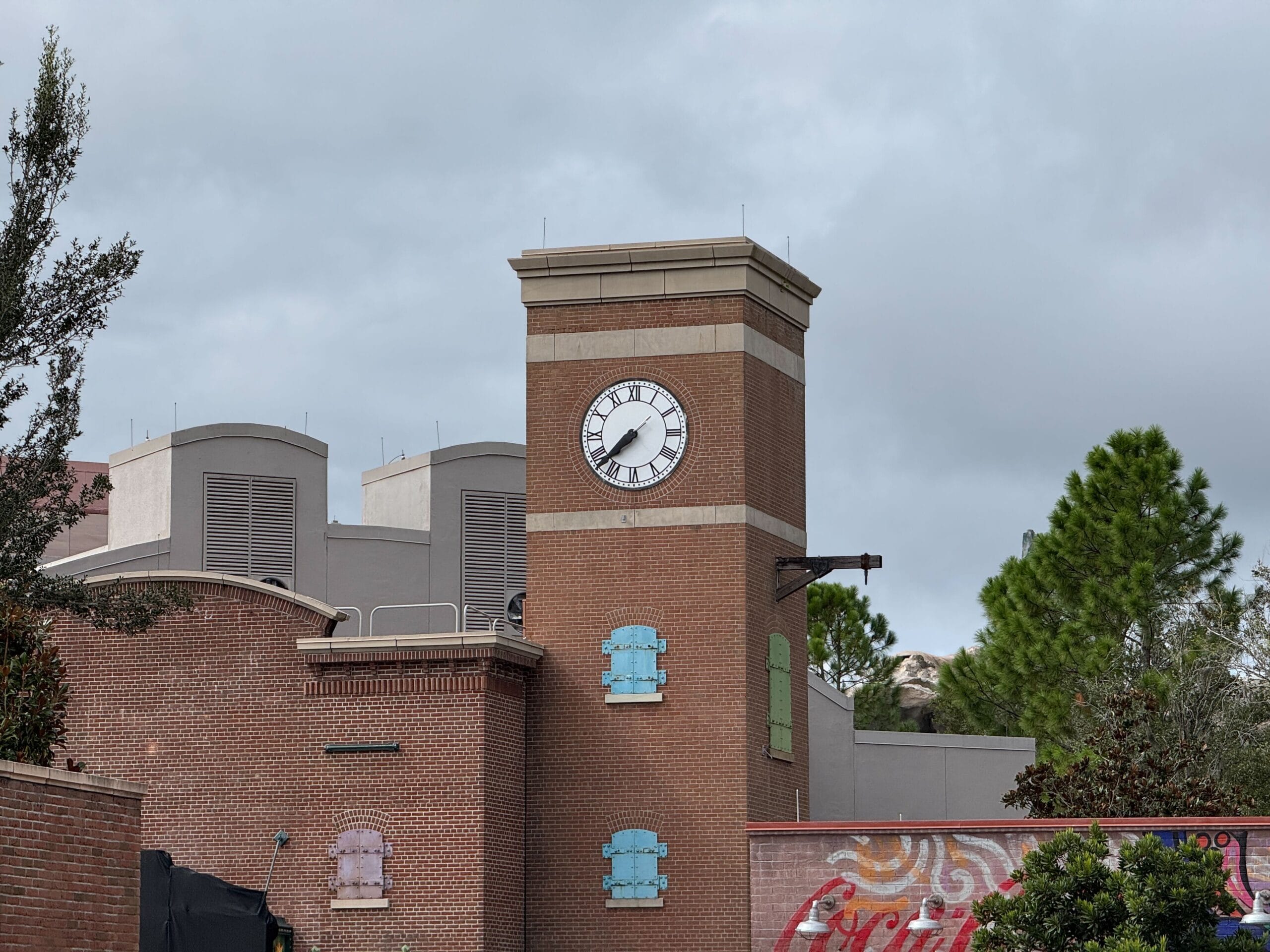 A brick clock tower shows the time as 11:15, with colorful window shutters and trees in the background.