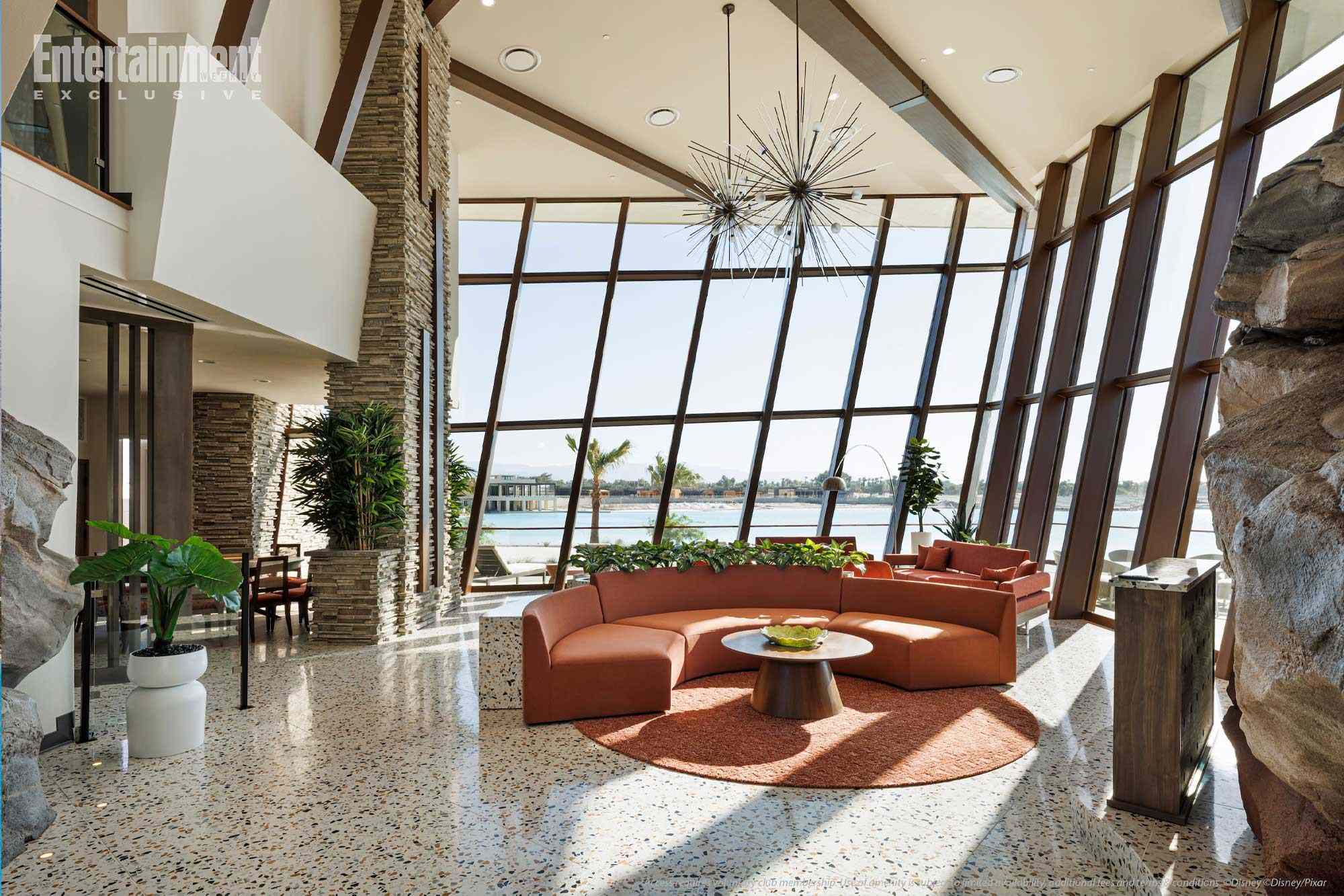 A modern lounge at Parr House with large slanted windows, orange curved sofas, lush plants, and water views—no Disney castle in sight.