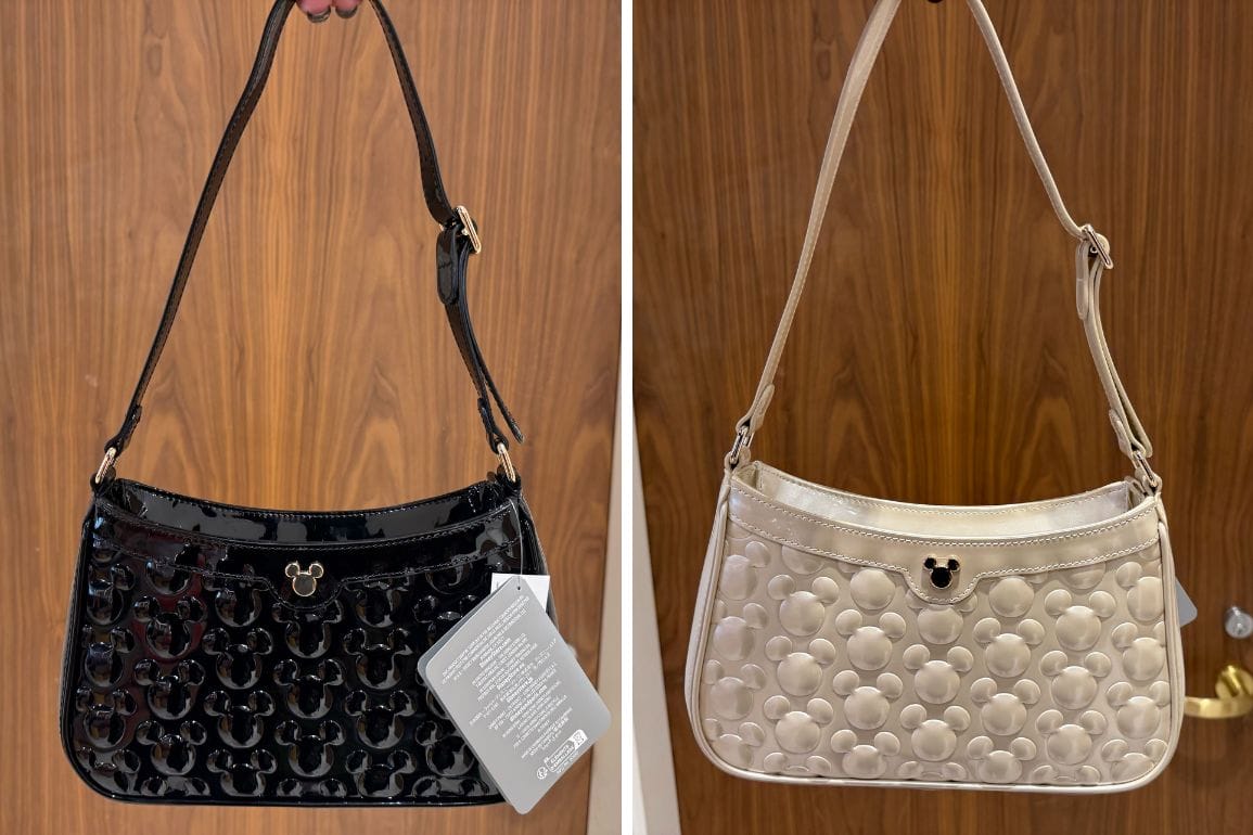 Two Disney park-inspired purses with Mickey Mouse patterns, one black and one cream, hang in front of a wooden backdrop.