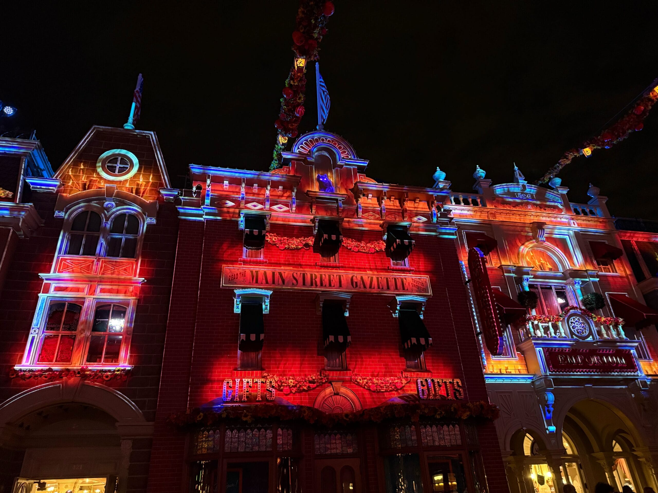Main Street building at Disneyland Paris lit up at night, featuring signs and a Halloween Projection Show.