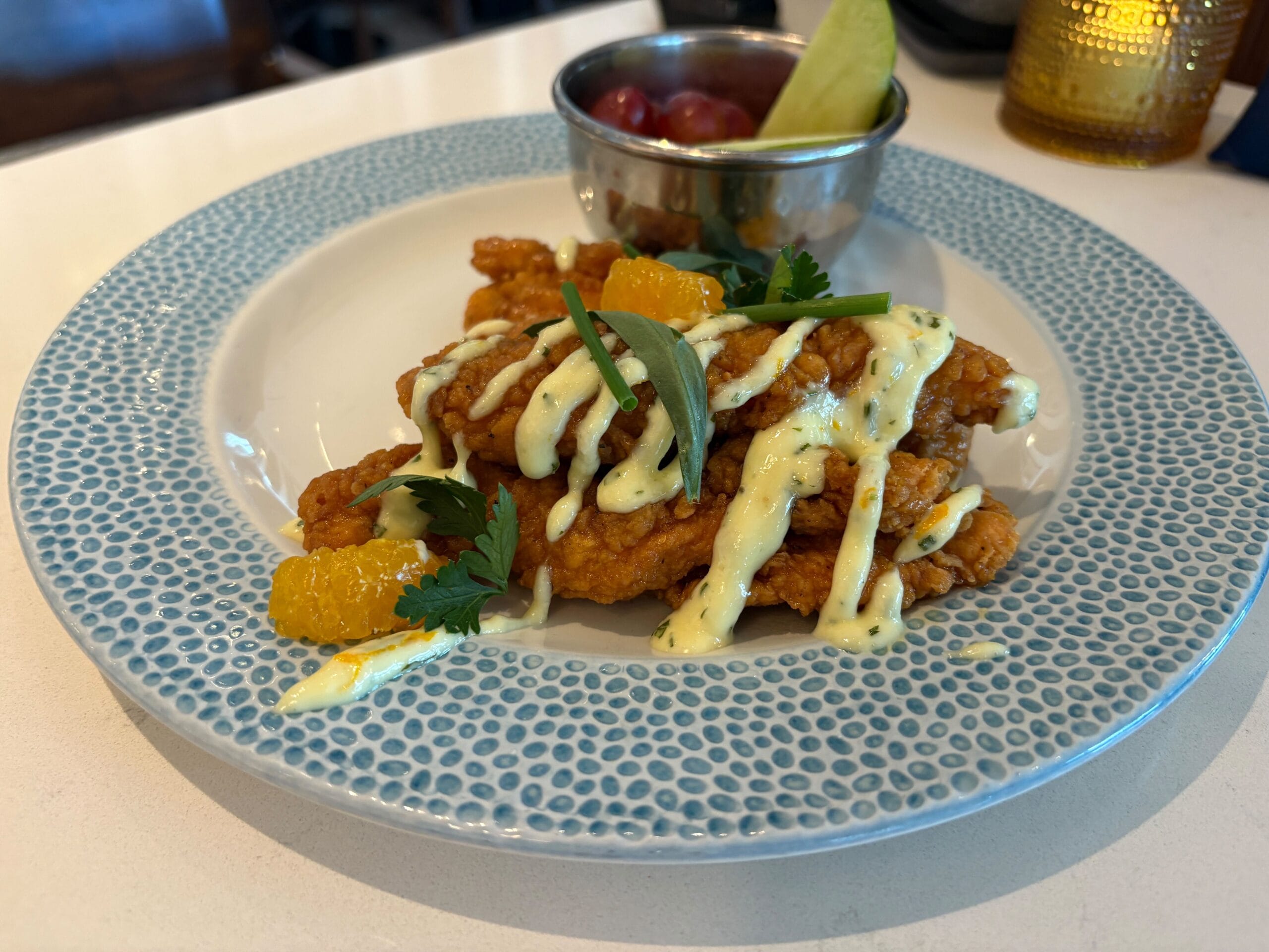 Citrus-glazed chicken strips with creamy sauce and fruit on a white and blue plate, a vibrant Disney parks-inspired meal.