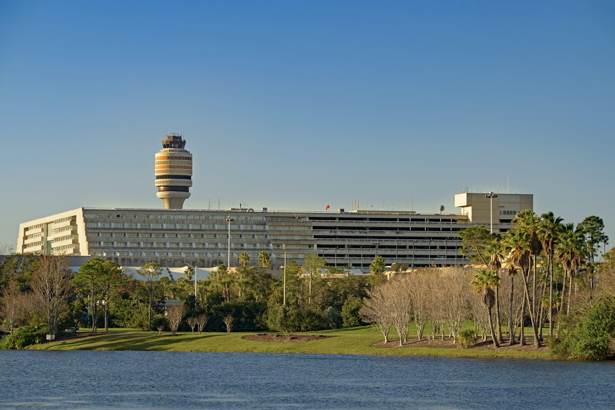 Orlando International Airport terminal and control tower, not a Disney castle, set amid trees and water under clear blue skies.