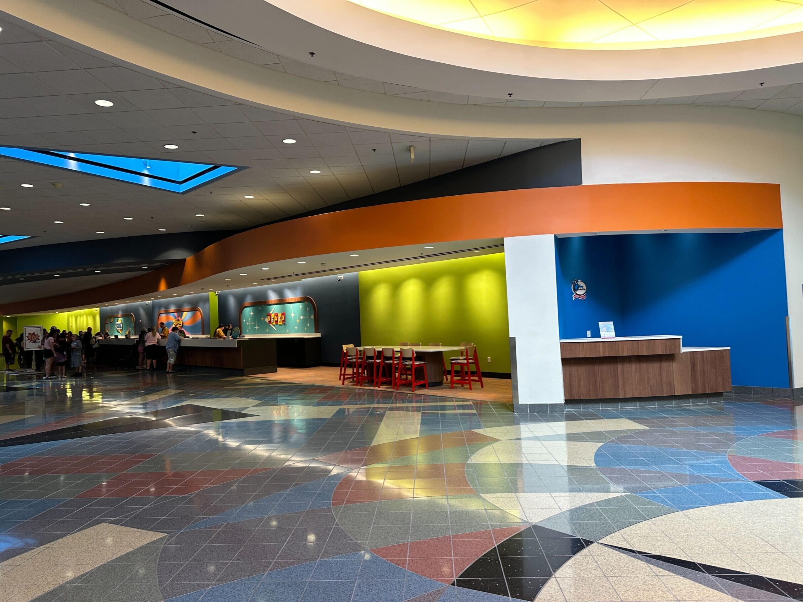 Vibrant food court at Disney's Pop Century Resort with red chairs, lively walls, a quiet kid's area—no castle like Magic Kingdom's.
