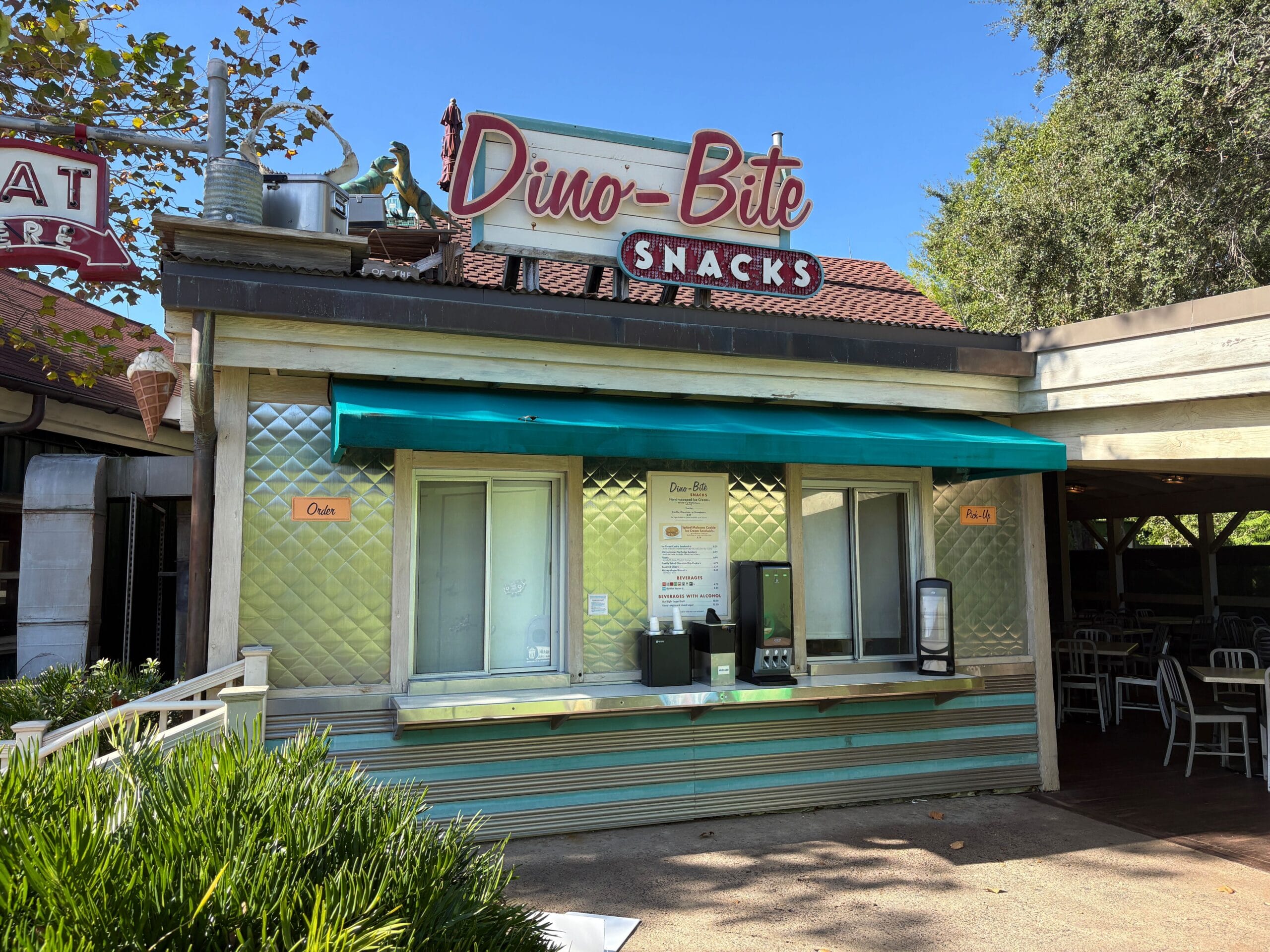 A shuttered Dino-Bite Snacks stand with metallic walls and teal awning in lush Disney's Animal Kingdom, no castle in sight here.