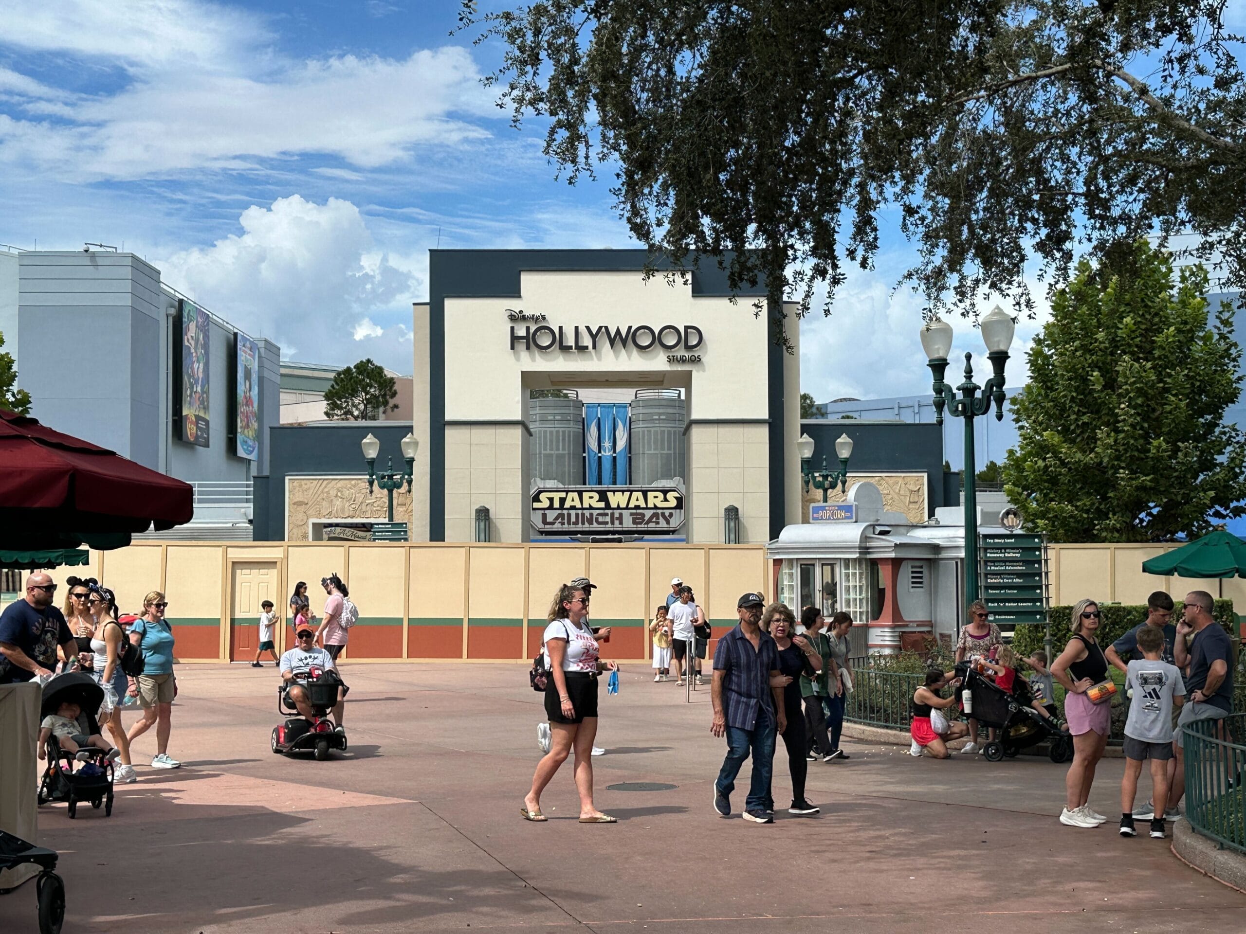 Guests stroll past Animation Courtyard by Star Wars Launch Bay at Disney’s Hollywood Studios, clouds overhead—no castle in view.