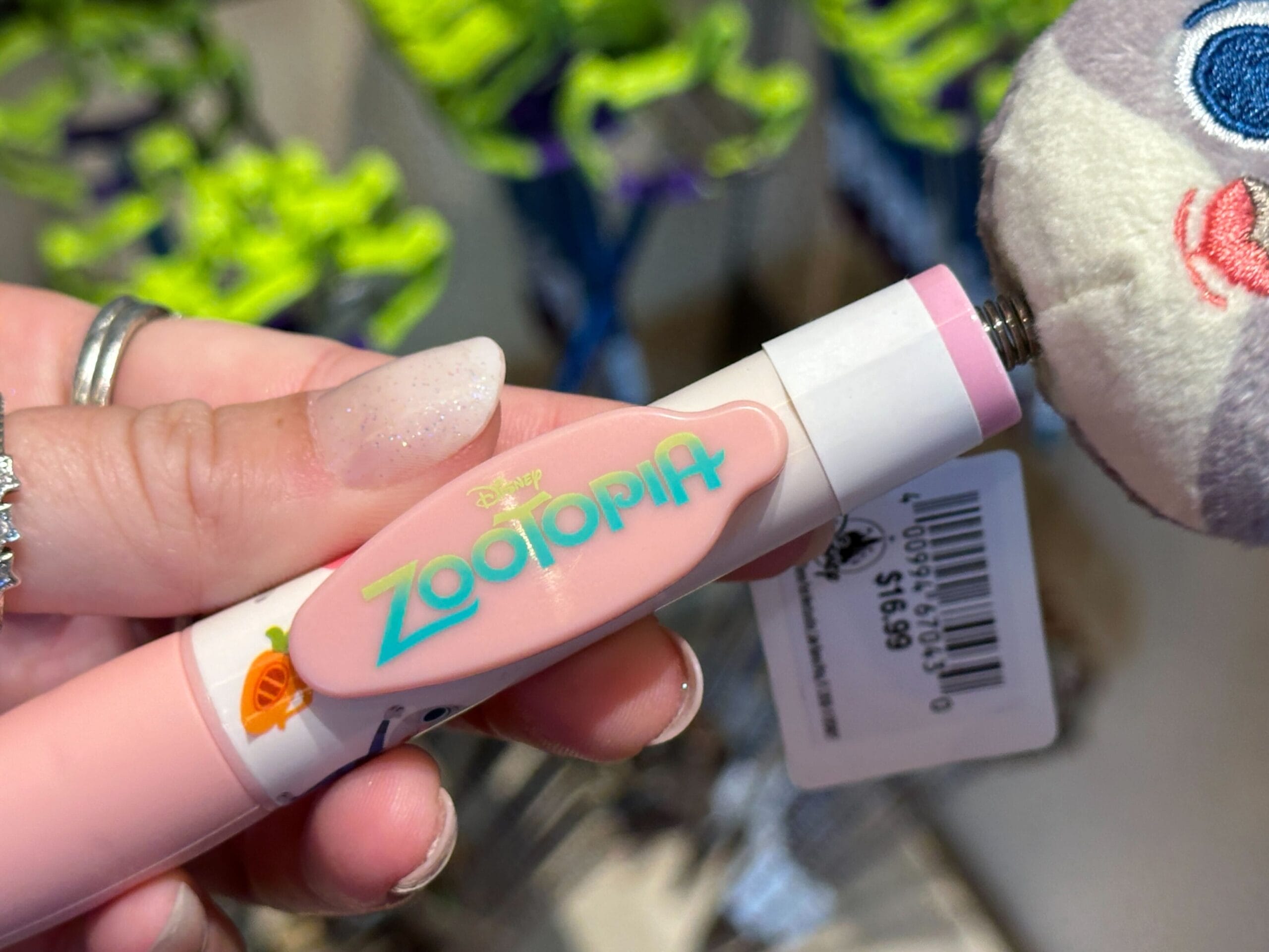 At a Disney Park shop, a hand holds a pink Zootopia pen by a plush toy with price tag—adorable stationery, park exclusive.