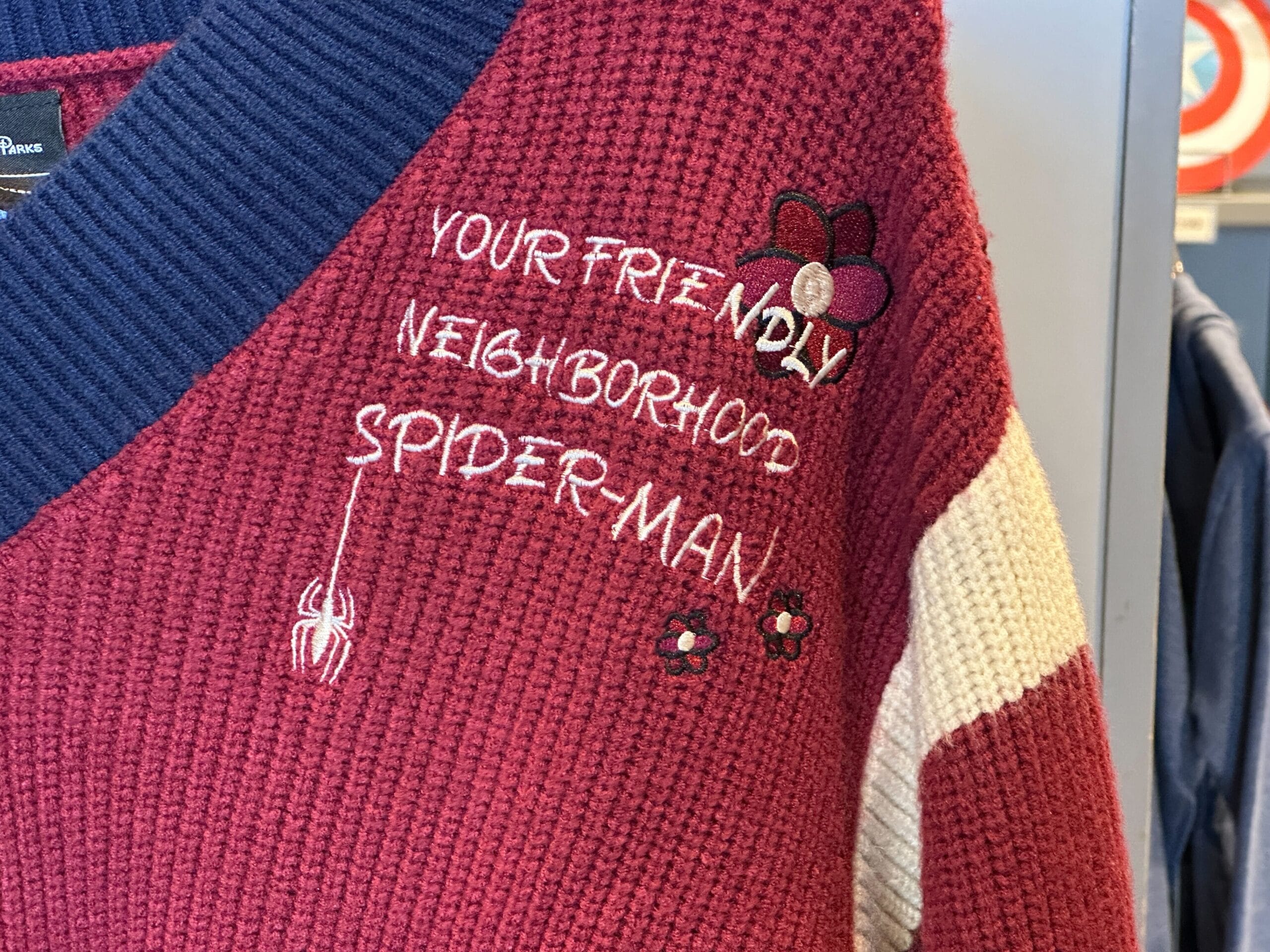 Red and cream Her Universe sweater with blue collar, Spider-Man designs and friendly text, seen at Disney parks, no castle present.