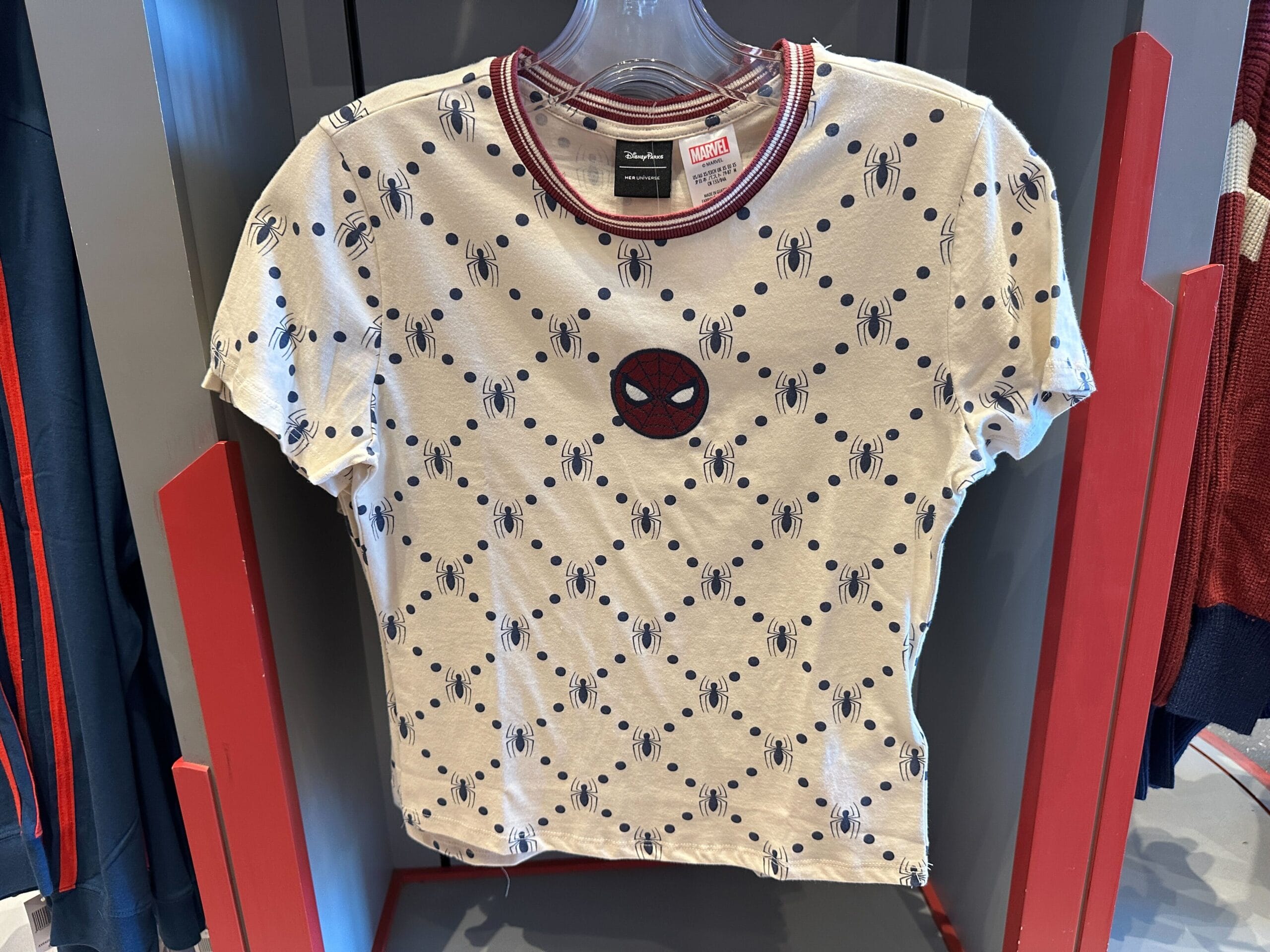 White tee with tiny black spiders and a red Spider-Man face patch; ideal Marvel apparel for Disney Parks, no castle imagery.