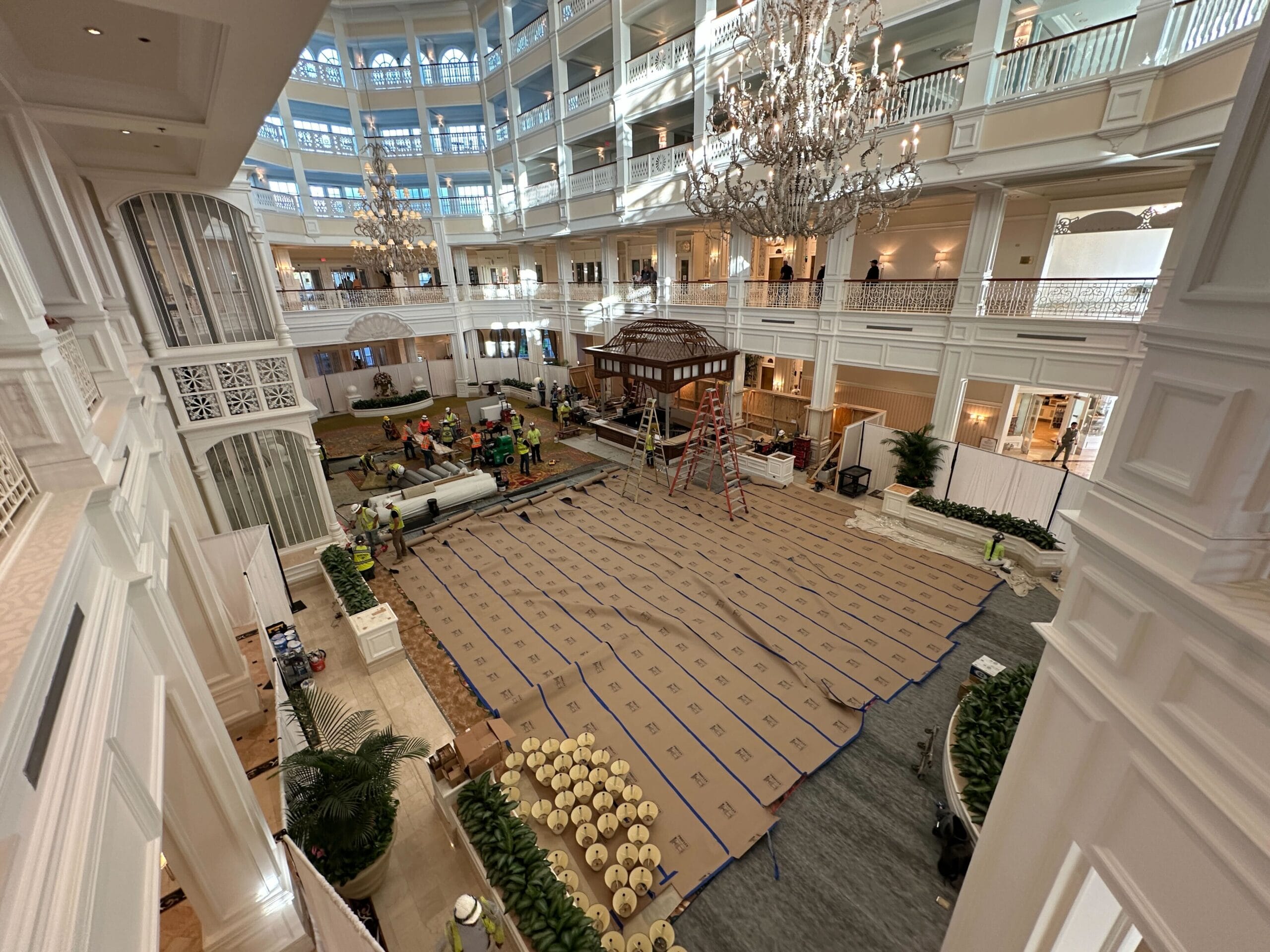 Workers prepare painting equipment, covering the Grand Floridian Lobby’s floor beneath soaring ceilings and sparkling chandeliers.