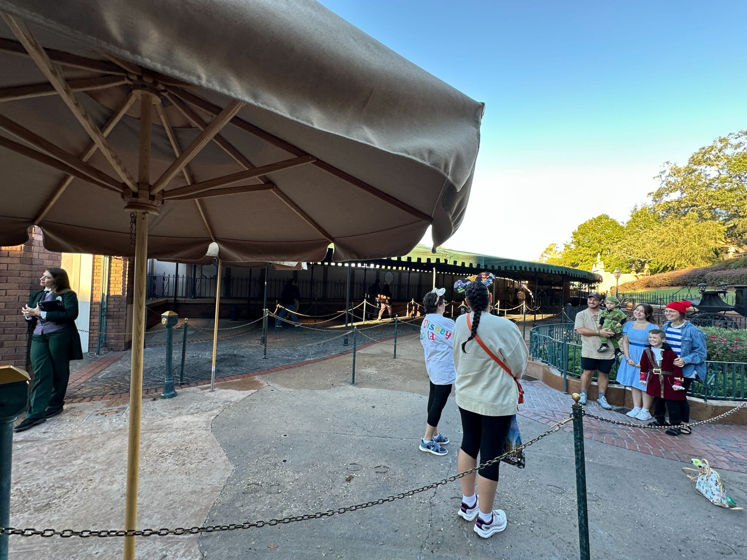 Guests line up near an umbrella as a family poses by the Haunted Mansion at Walt Disney World, not in front of any park castle.