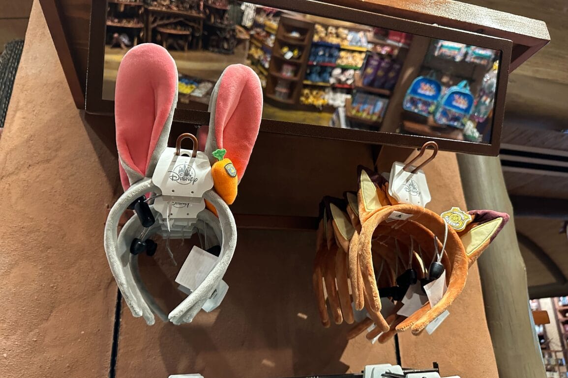 Judy and Nick Ears headbands with bunny and fox designs, displayed in a lively Disney park shop reminiscent of Main Street stores.