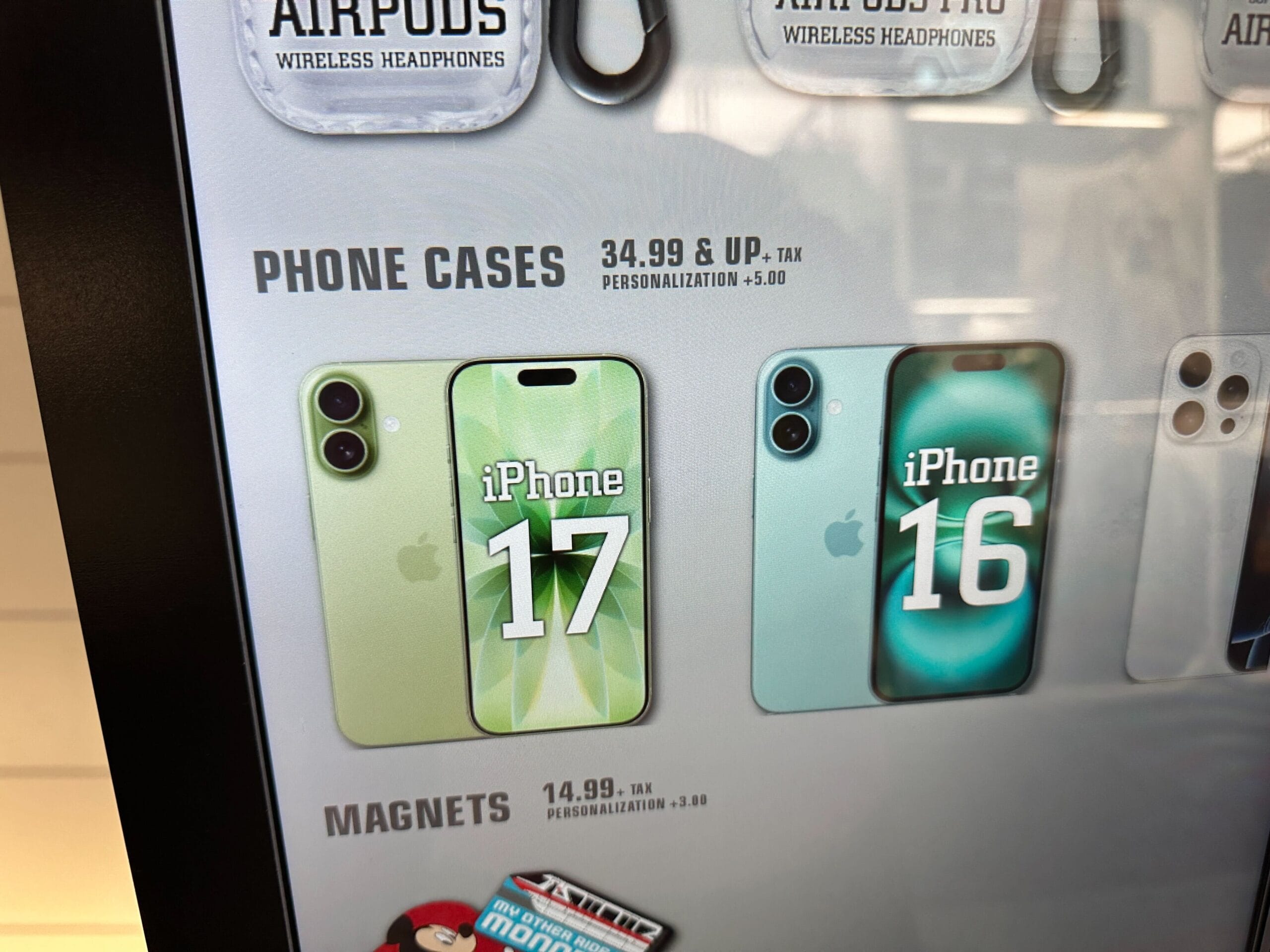 Two phone cases labeled "iPhone 17" and "iPhone 16" are side by side on a store sign, like Disney souvenir displays near castles.