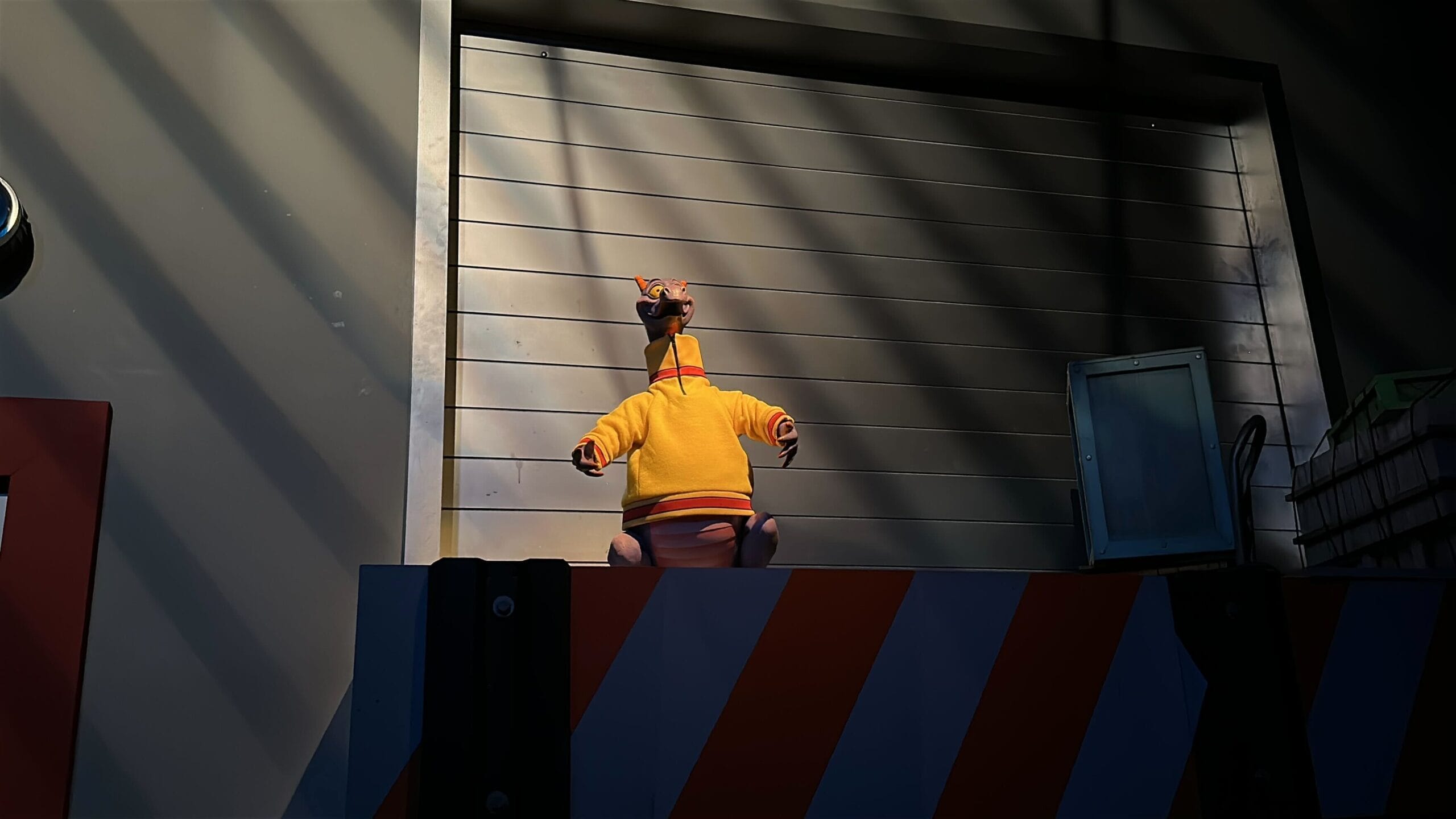A toy giraffe in a yellow hoodie sits on a ledge, evoking classic Disney park nostalgia like Figment at Epcot's Imagination Pavilion.
