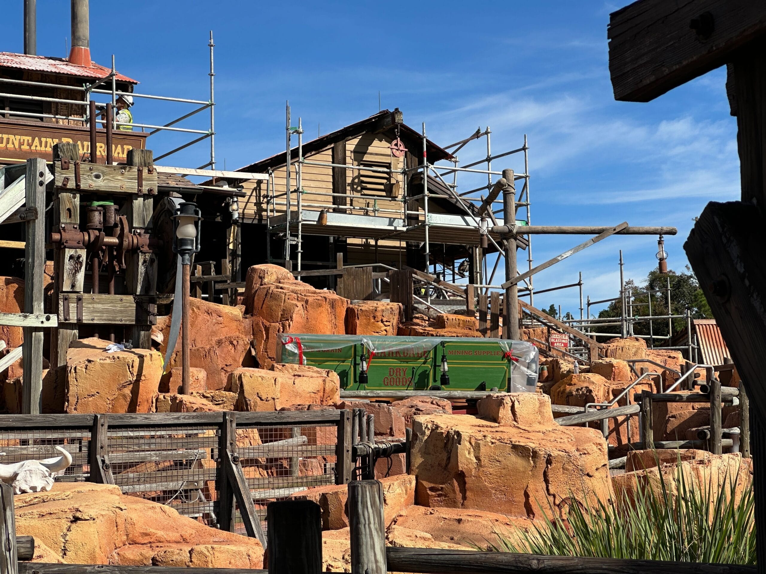 Disney park attraction under construction with scaffolding, rustic wood buildings, and Big Thunder-style orange rockwork in front.