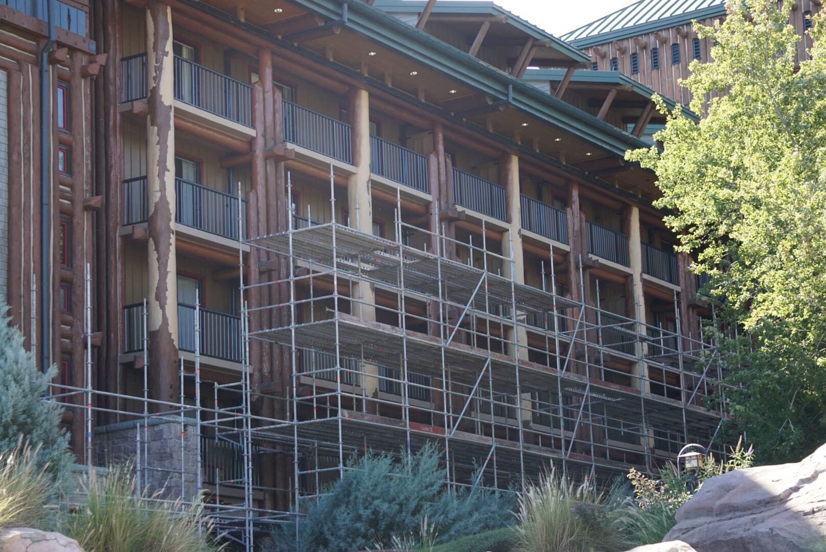 Scaffolding covers a multi-story lodge with balconies, surrounded by greenery, resembling Disney’s Wilderness Lodge at Walt Disney World.