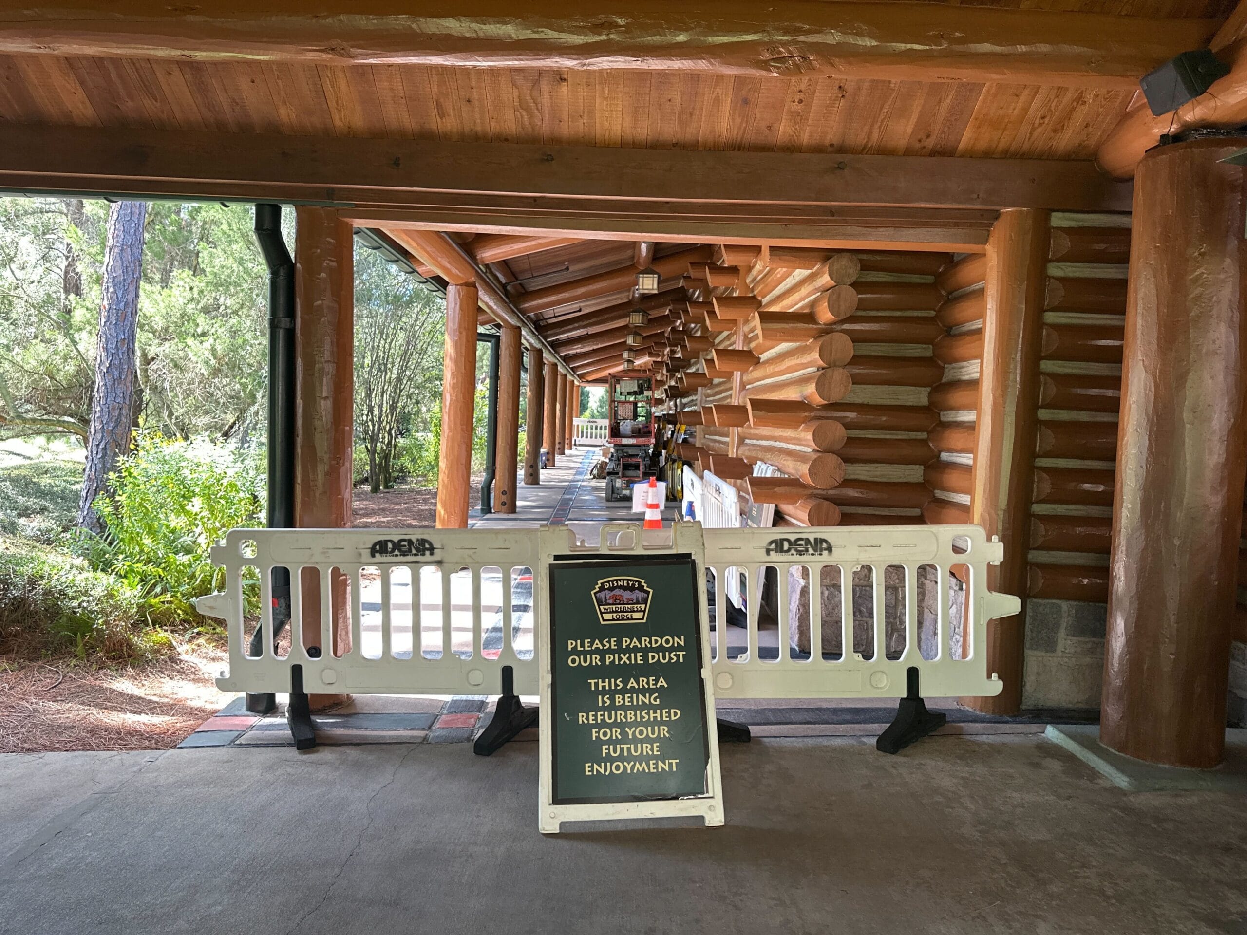 White construction barriers block a wooded walkway in a Disney park, with a sign about refurbishment for future guest enjoyment.