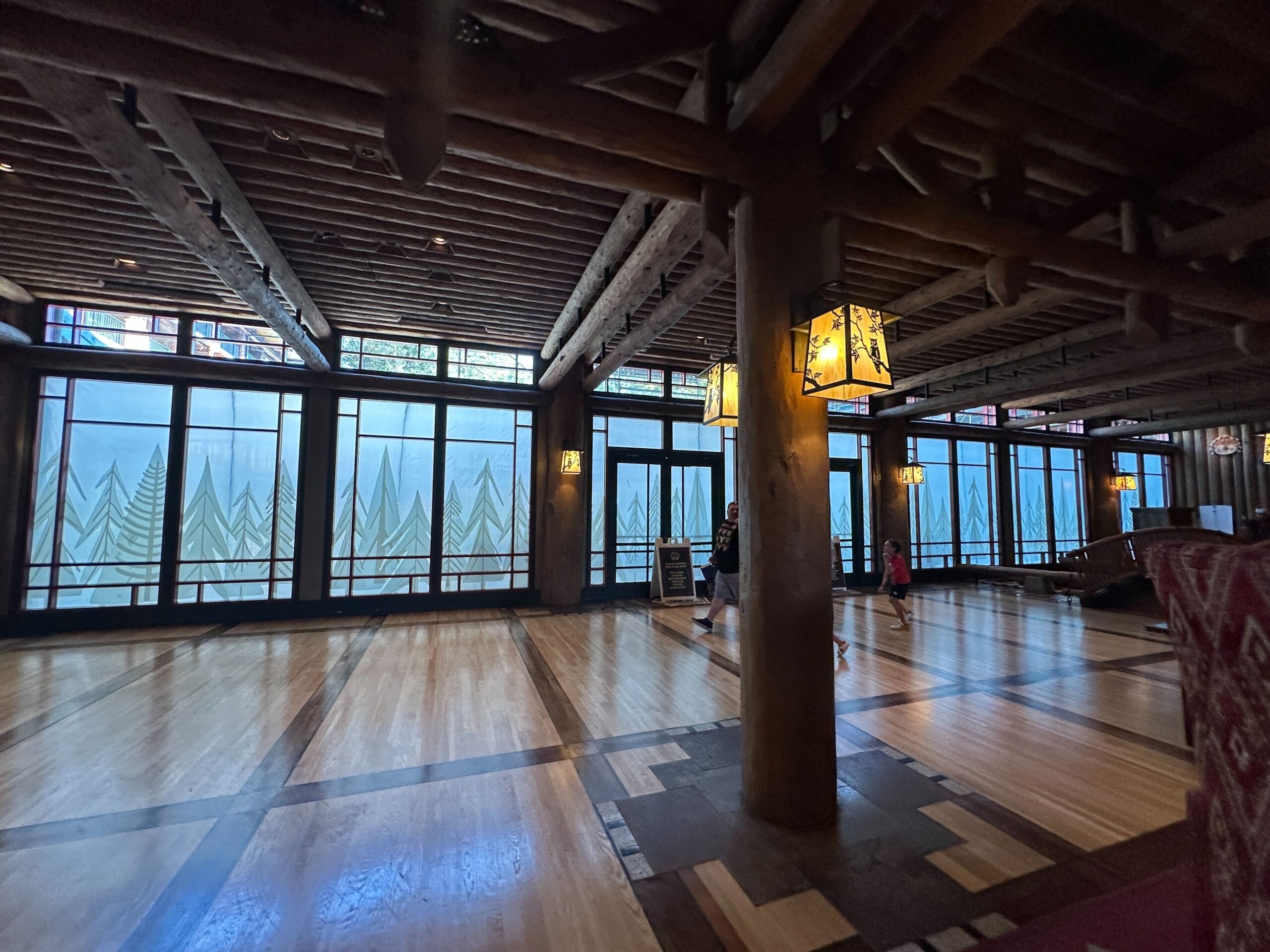 Inviting lodge lobby in Disney style, with rustic wooden beams, nature-inspired windows, soft lantern lighting, and guests strolling.