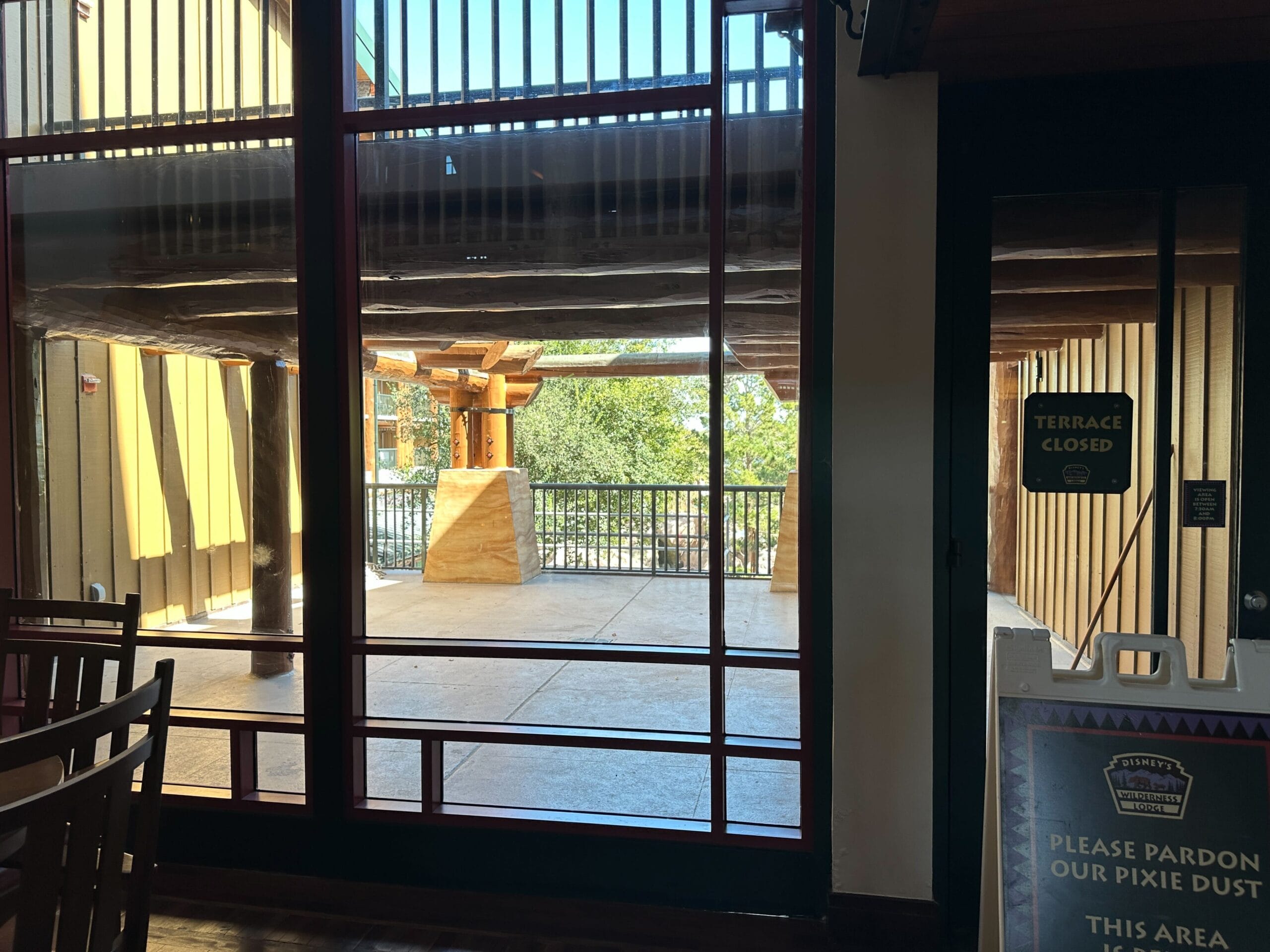 A sunlit terrace at a Disney park is closed off behind glass doors, with a "Terrace Closed" sign and construction notice visible.