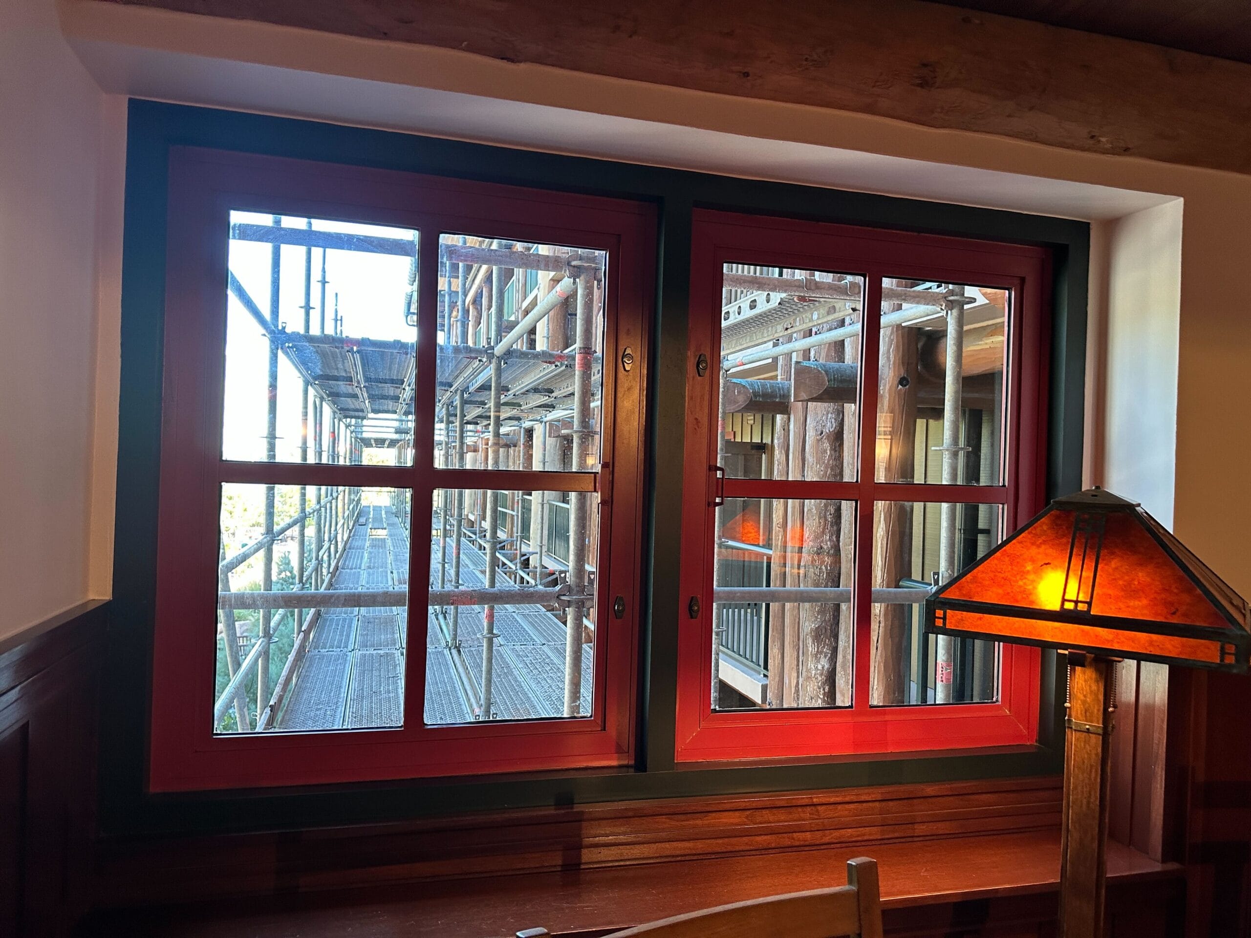 Looking through a red-trimmed window—similar to Main Street facades at Disneyland—shows scaffolding outside, desk and lamp inside.