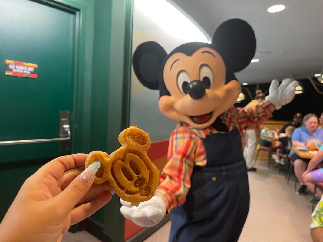 Hand holds Mickey waffle in front of Mickey at Garden Grill in EPCOT