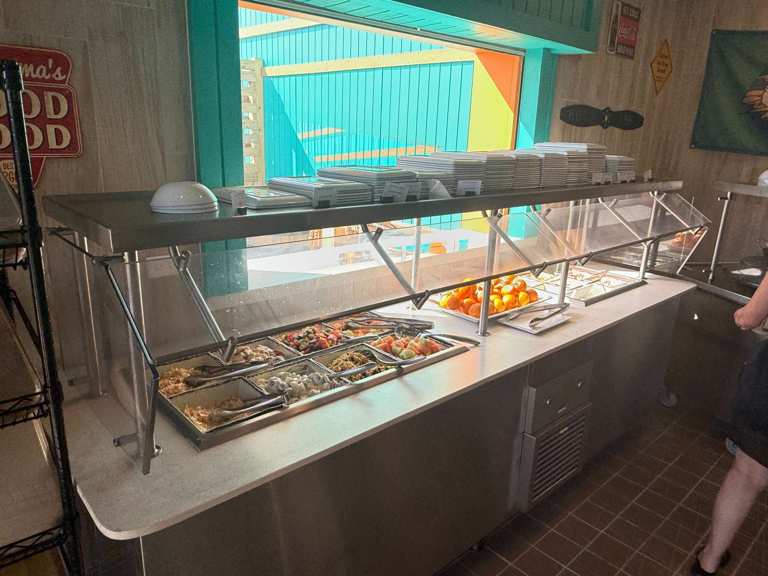 There are small signs labels above the food trays, along with stacks of plates and bowls.