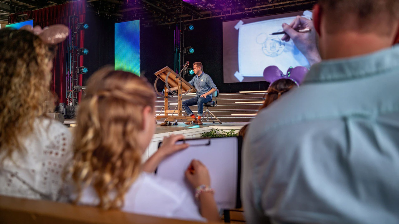 A man on stage using a projector to share a live illustration of Mickey Mouse for an audience