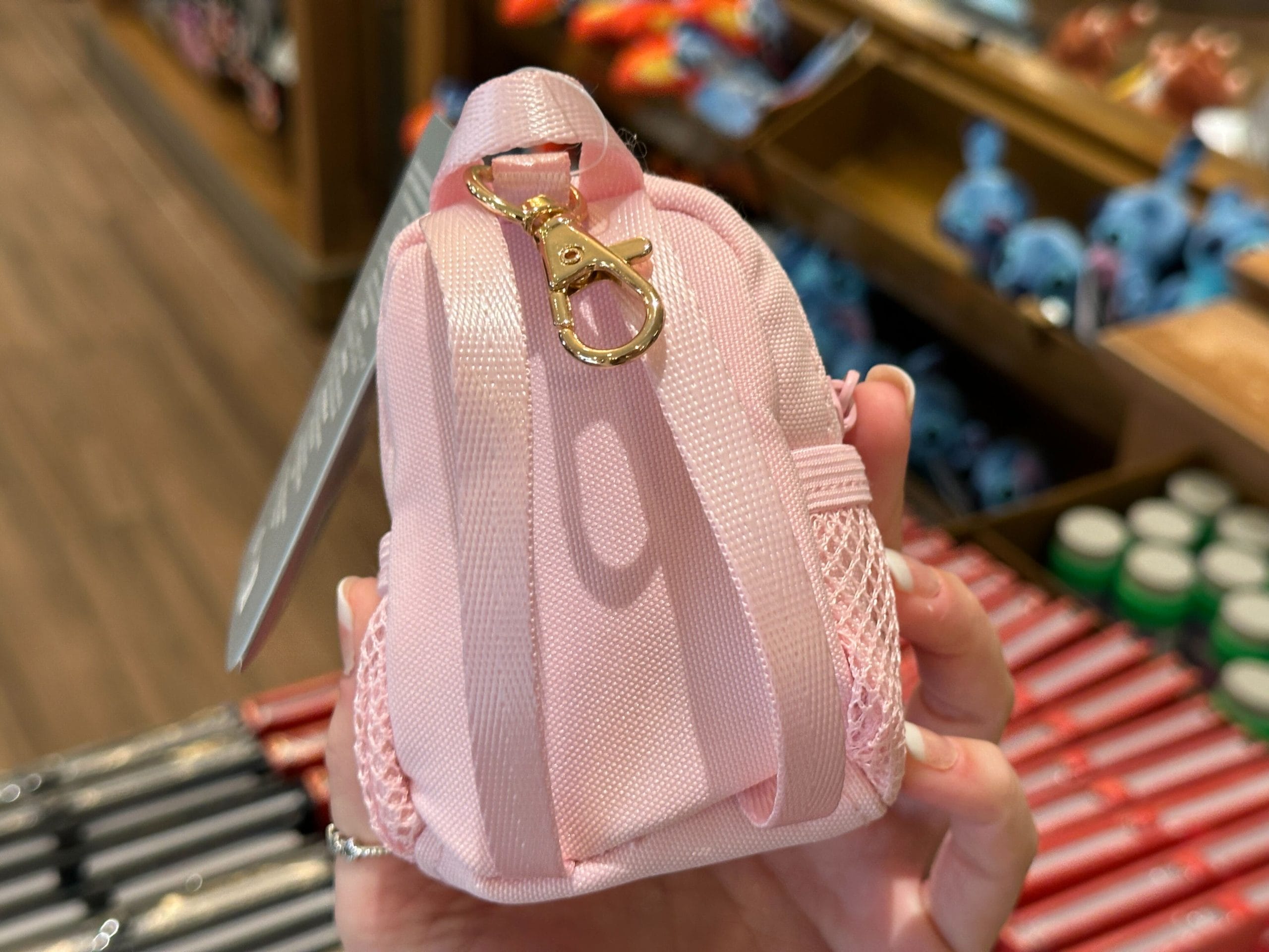 A hand holds a small pink backpack keychain charm with a white Walt Disney World "D" logo.