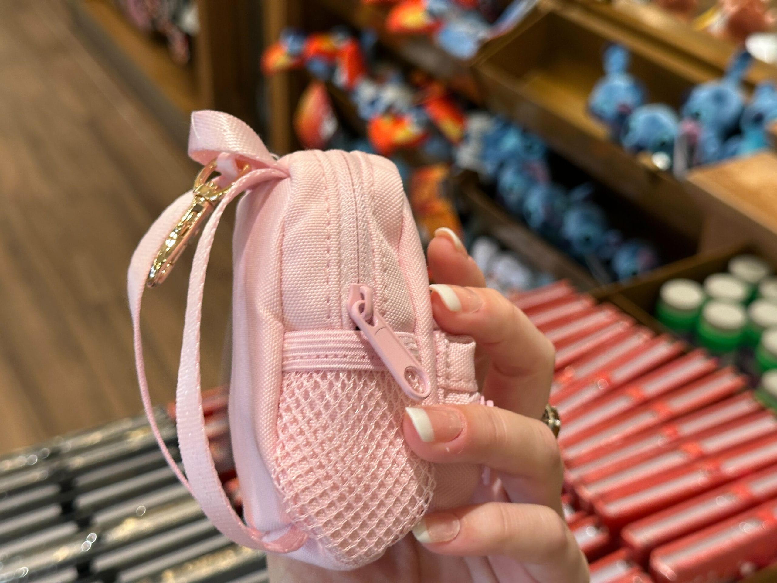 A hand holds a small pink backpack keychain charm with a white Walt Disney World "D" logo.