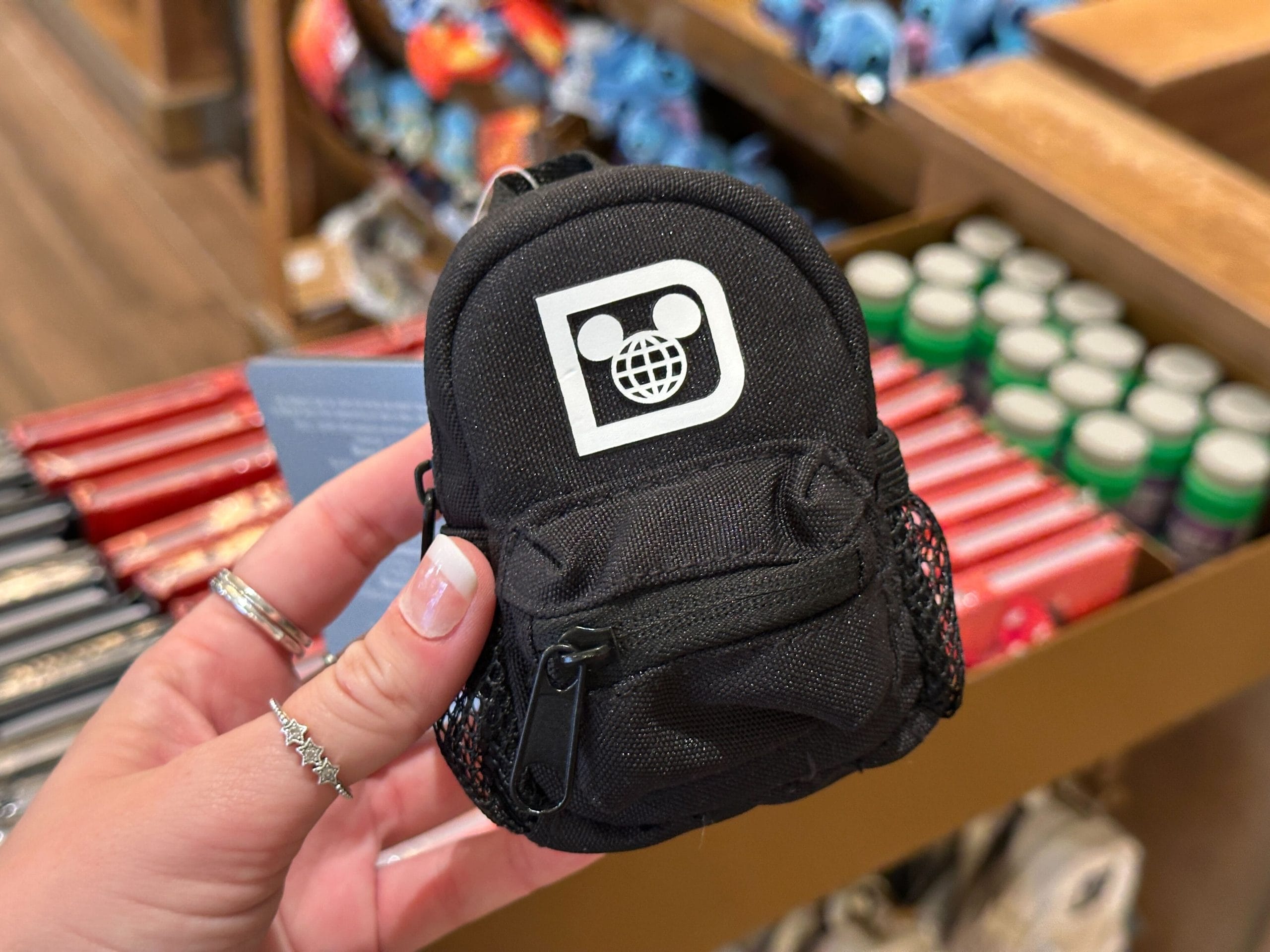 A hand holds a small black backpack keychain charm with a white Walt Disney World "D" logo.