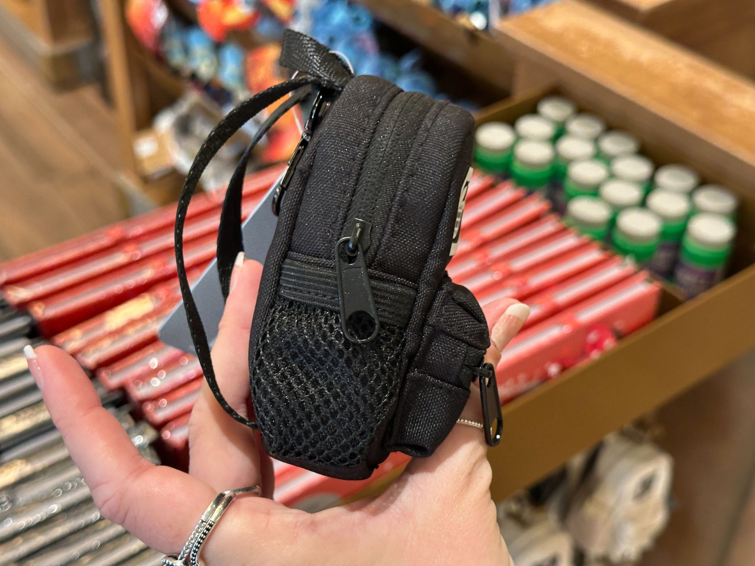A hand holds a small black backpack keychain charm with a white Walt Disney World "D" logo.