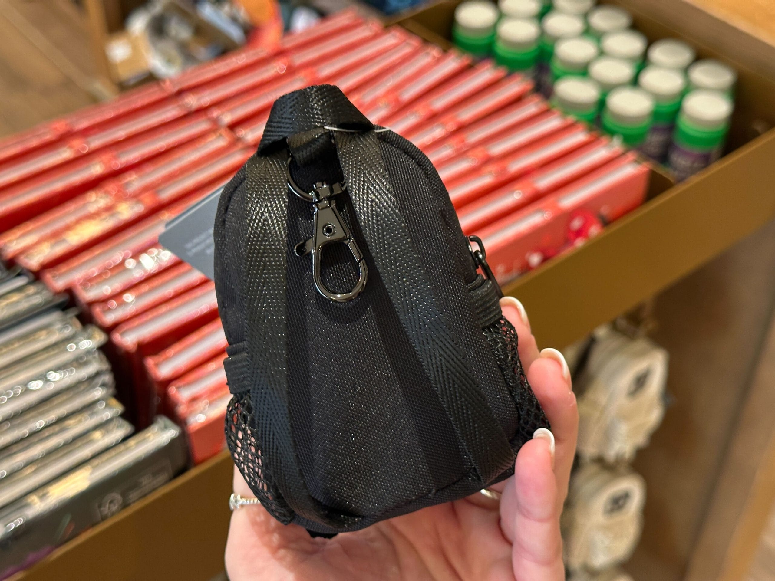 A hand holds a small black backpack keychain charm with a white Walt Disney World "D" logo.