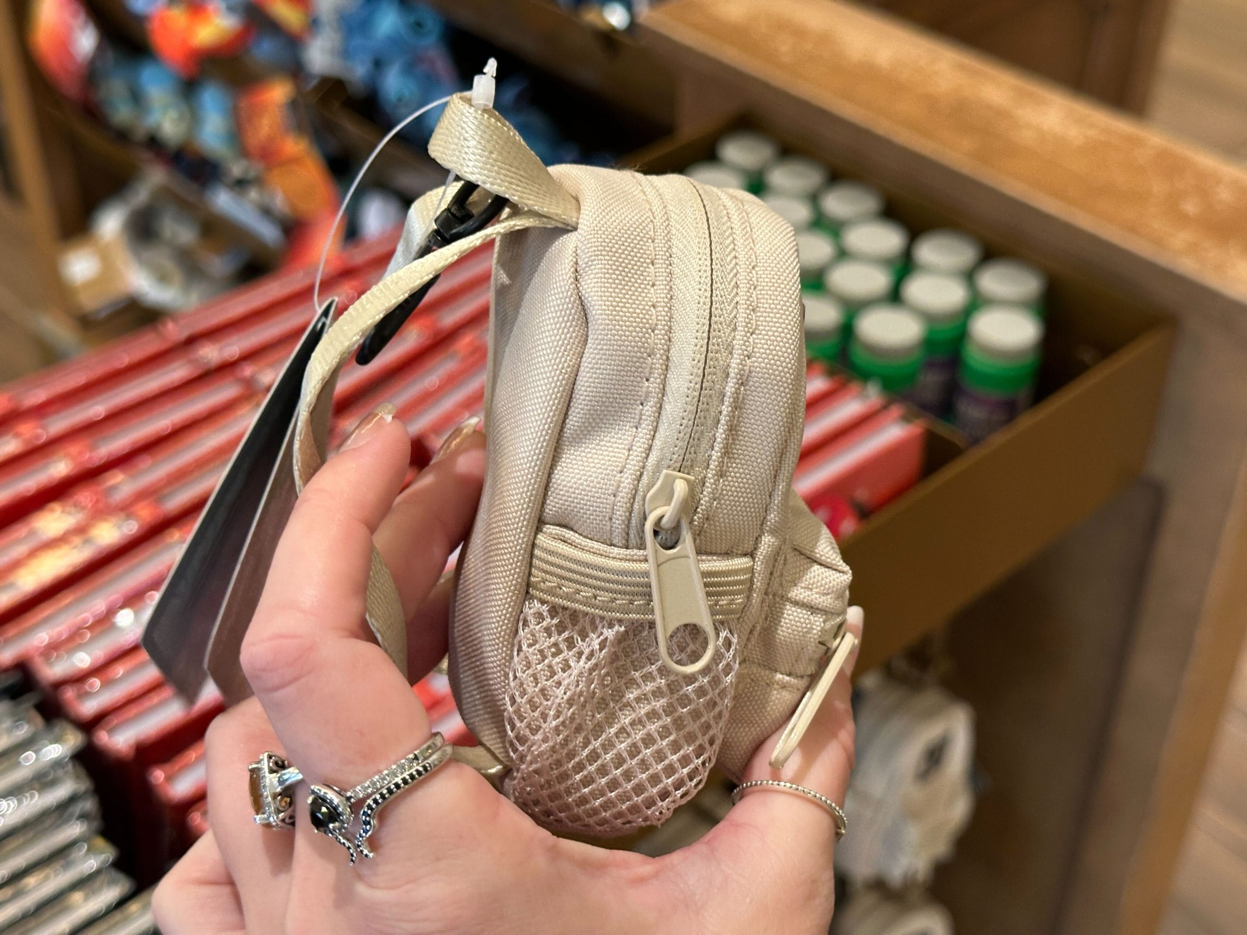 A hand holds a small white backpack keychain charm with a black Walt Disney World "D" logo.