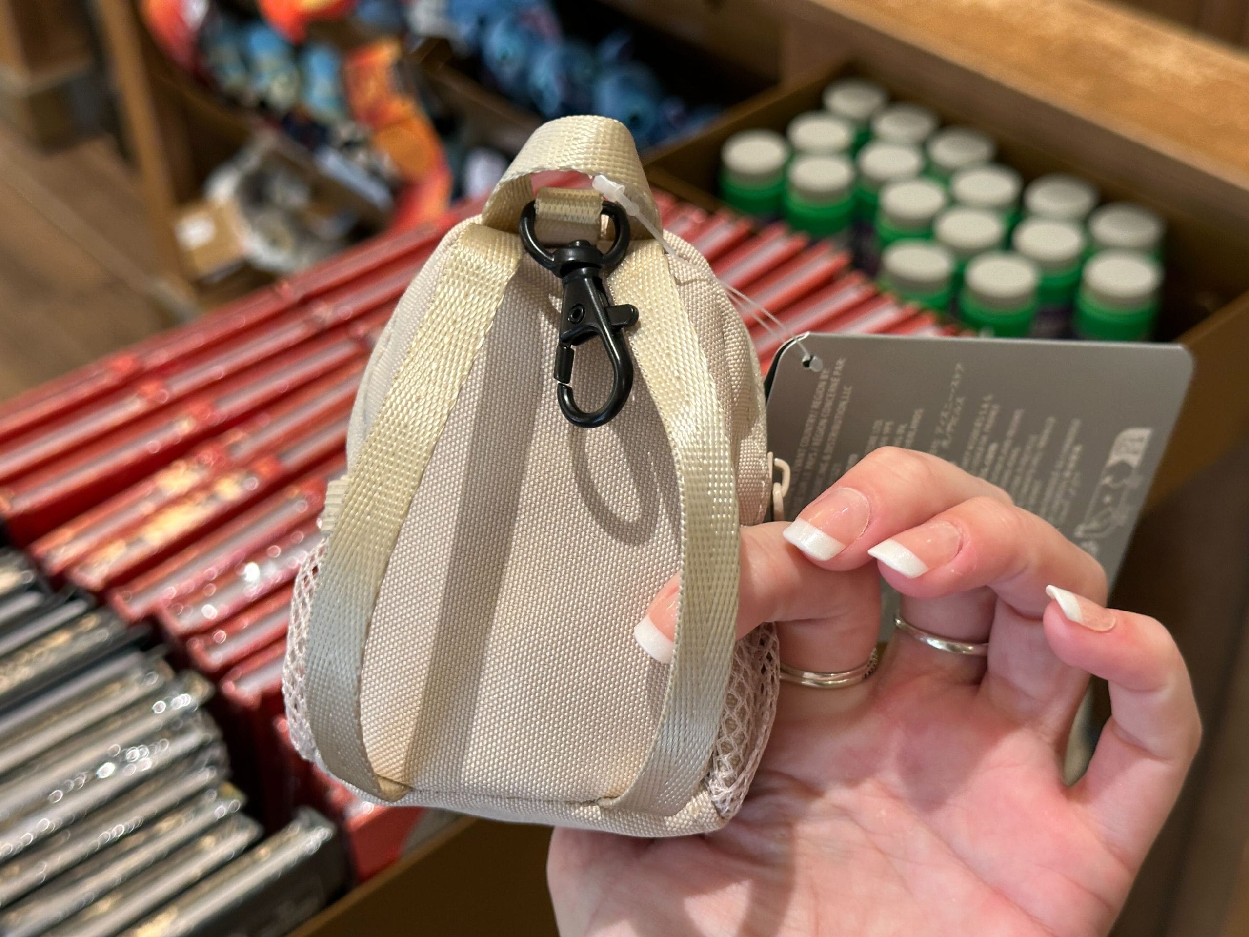 A hand holds a small white backpack keychain charm with a black Walt Disney World "D" logo.