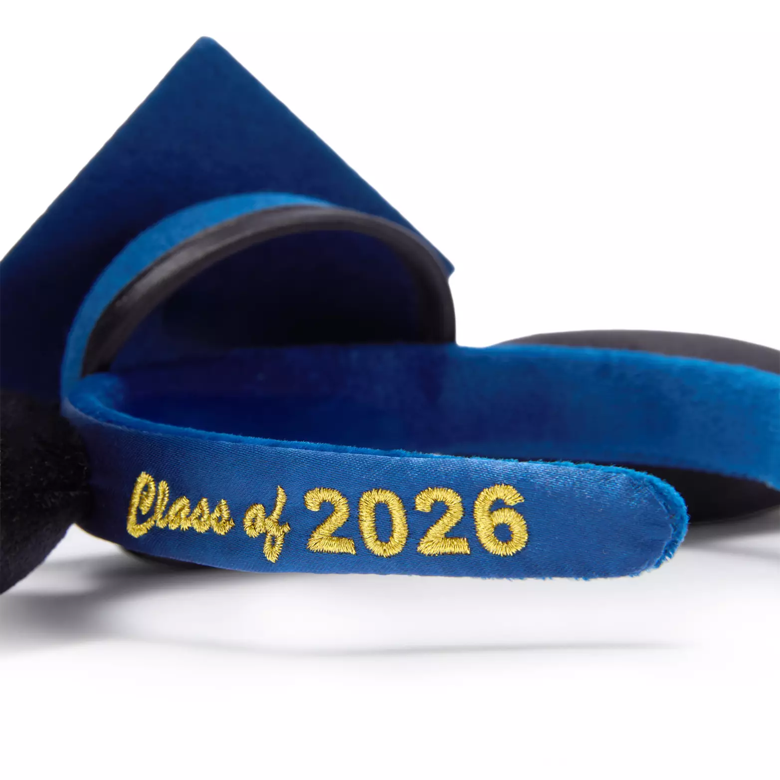 The black Mickey ears on this headband frame a blue graduation cap with black trim. The headband is also blue with "Class of 2026" embroidered in yellow-gold on one side. On the graduation cap is a gold tassel.
