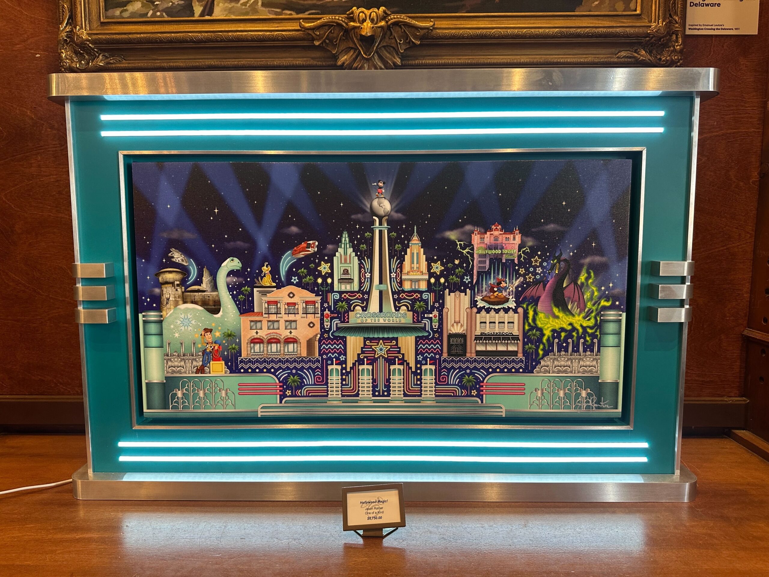 This one-of-a-kind art piece by Jason Ratner mimics the theming of the entrance to Disney's Hollywood Studios with its silver trim, aqua background, and blue neon lighting. The art piece showcases numerous iconic attractions from Disney's Hollywood Studios at night, including Fantasmic, the Twilight Zone Tower of Terror, the Crossroads of the World shop, Star Tours, Toy Story Land, Star Wars: Galaxy's Edge, and even Gertie the dinosaur.