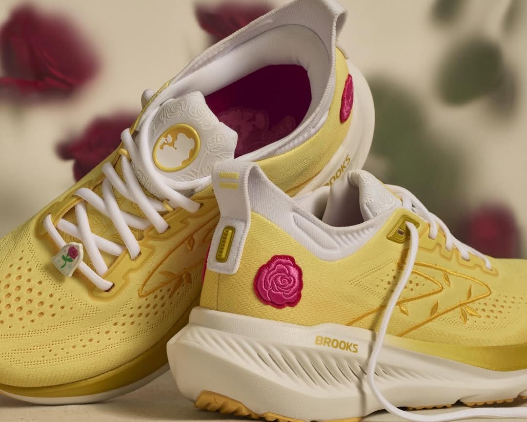 In canary yellow, these Brooks shoes are all about Belle. A silhouette portrait of Belle in yellow and gold is on the front of the shoe's tongue. The body of the shoes is yellow, while the base and laces are white. A red rose patch is placed on the back, outer ankle side of the shoes, and a lace decoration of the rose under a cloche is on the bottom of the front laces.