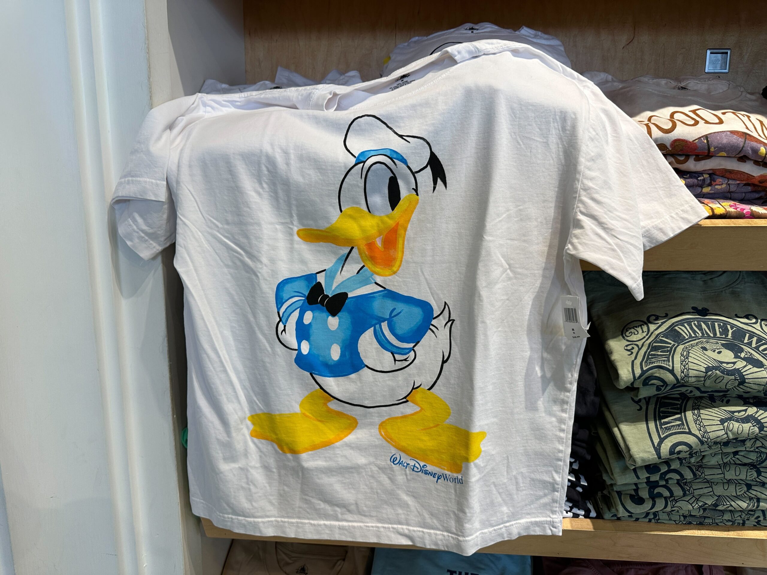 Donald Duck as he first appeared in The Wise Little Hen (1934) is on the chest of this light blue shirt. Compared to his modern design, he has a longer, thinner bill. But he's still wearing his iconic blue sailor suit and hat.