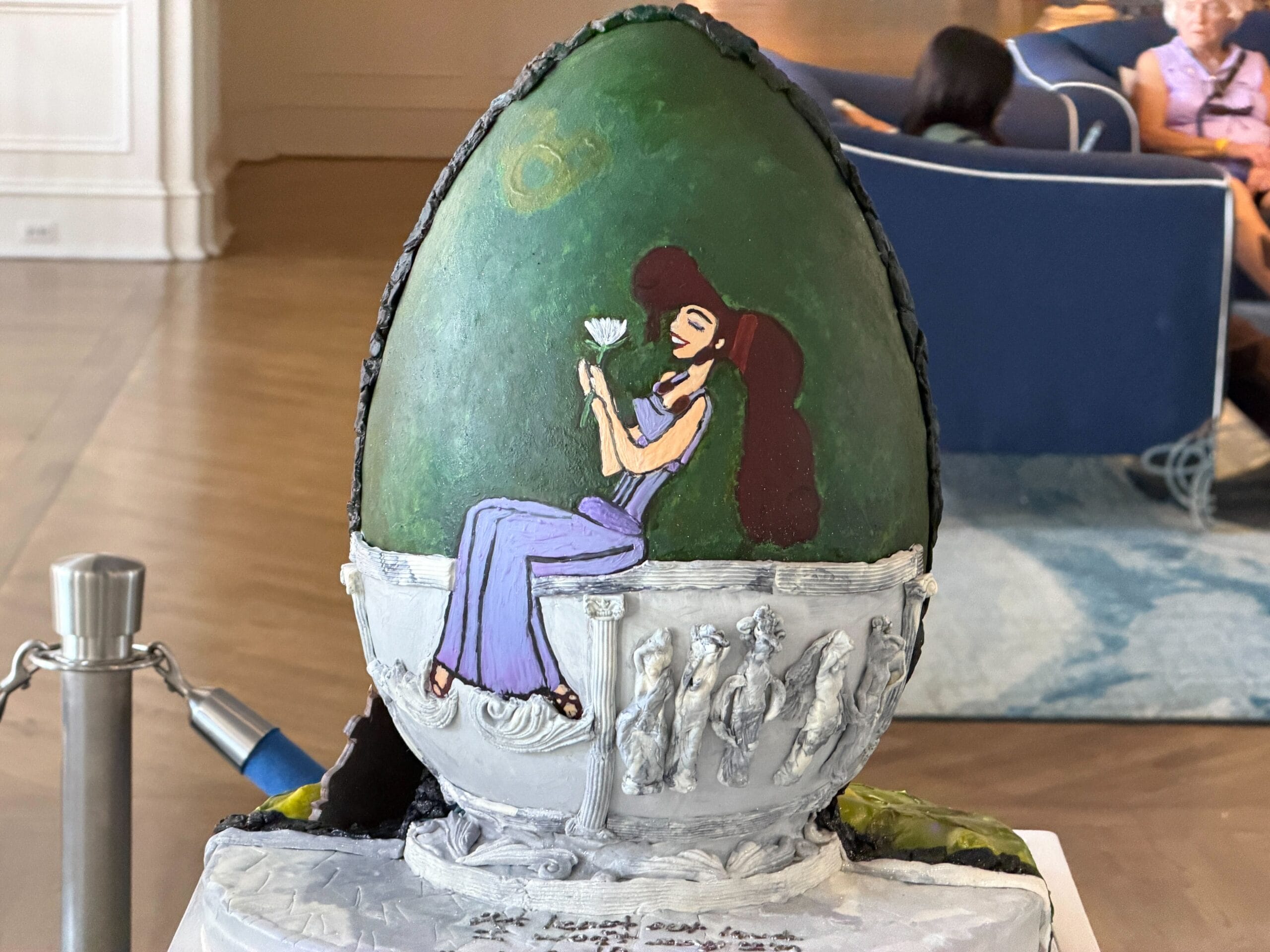 The back of the egg has a painted picture of Megara sitting on top of a bench. The muses are represented on the bench as Megara holds a white flower as a reference to 'I won't say I'm in love.'