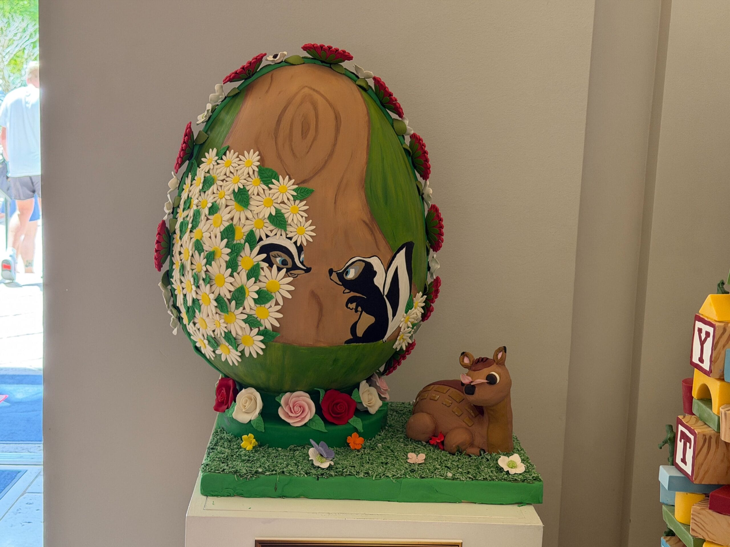The second egg is a display of the film Bambi. Bambi himself is lying at the base with a butterfly resting on his nose. The egg features a painted display of Flower meeting Petunia, while white, pink, and red roses surround the frame and bottom of the egg.