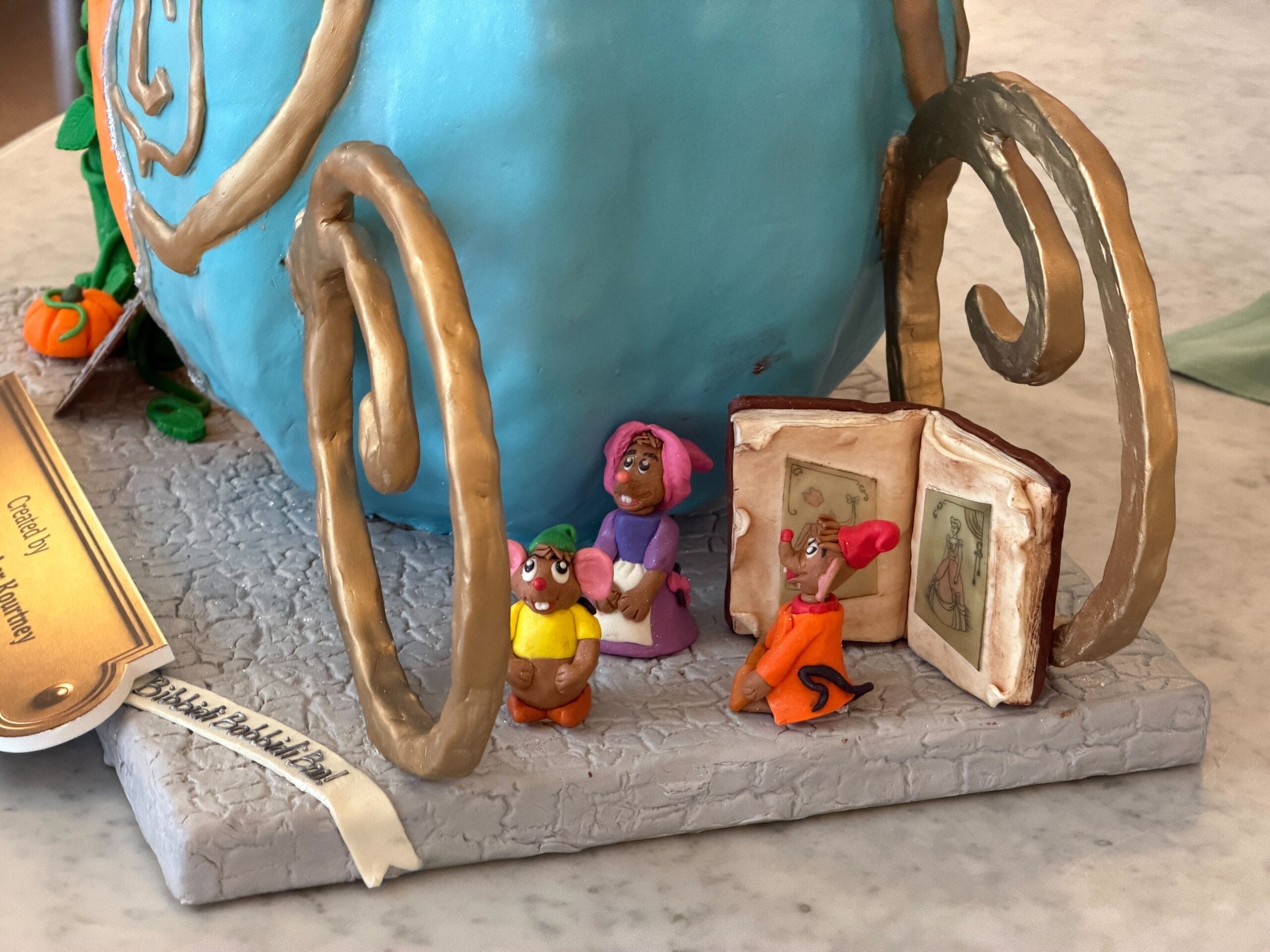 Jaqcues, Gus, and Mary, the mice from the film, as they are reading the book from which they make Cinderella's dress. Bibbity Bobbity Boo! is written on the ground, while another sign reads Pumpkin Patch! next to the glass slipper sitting on a pillow.